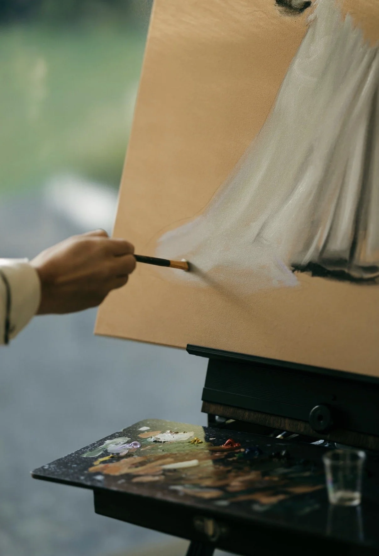 An artist's hand painting a portrait on a canvas, with a palette of paints and brushes nearby.