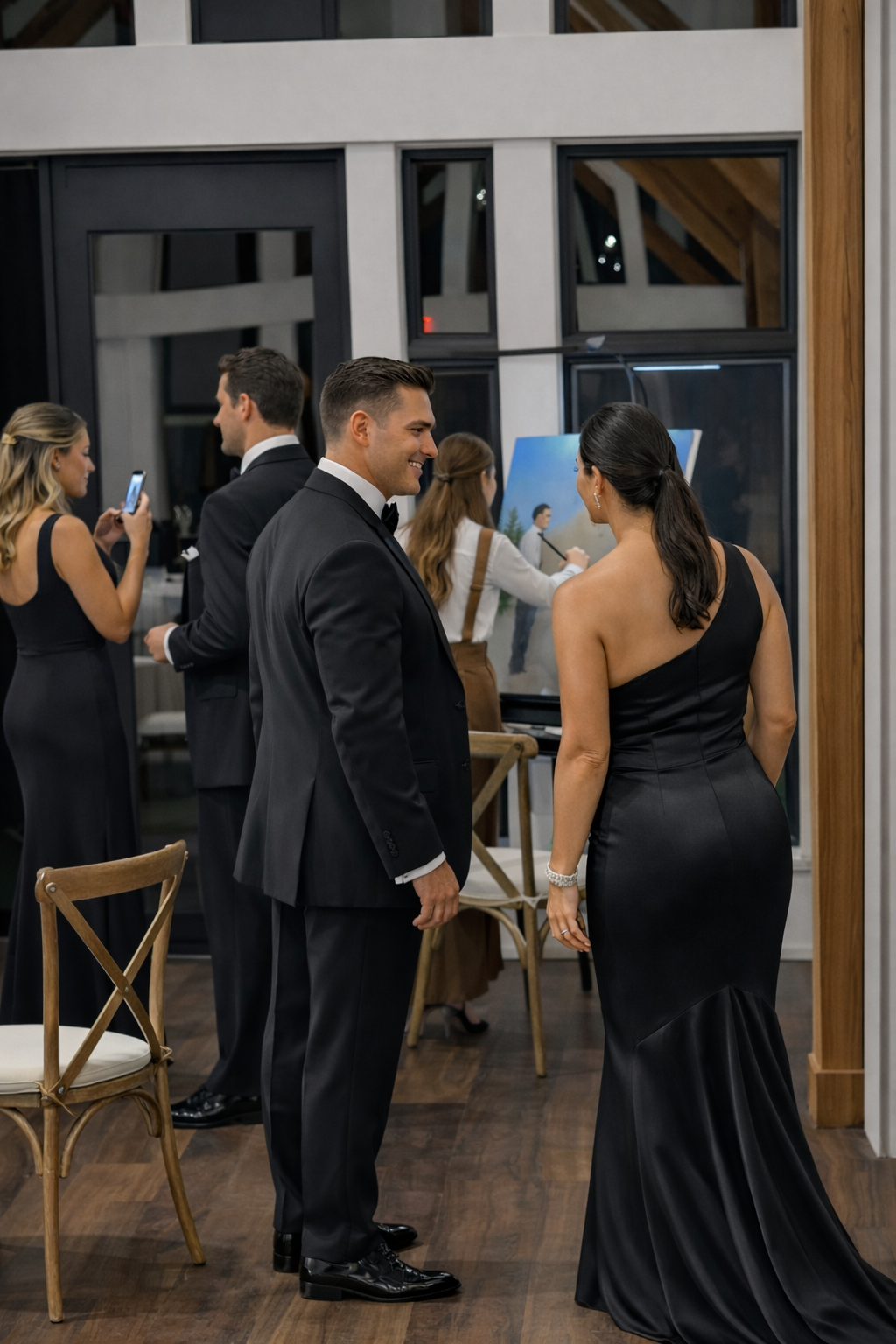 A man and woman in formal attire talking at an indoor event, with other guests and an artist painting in the background.