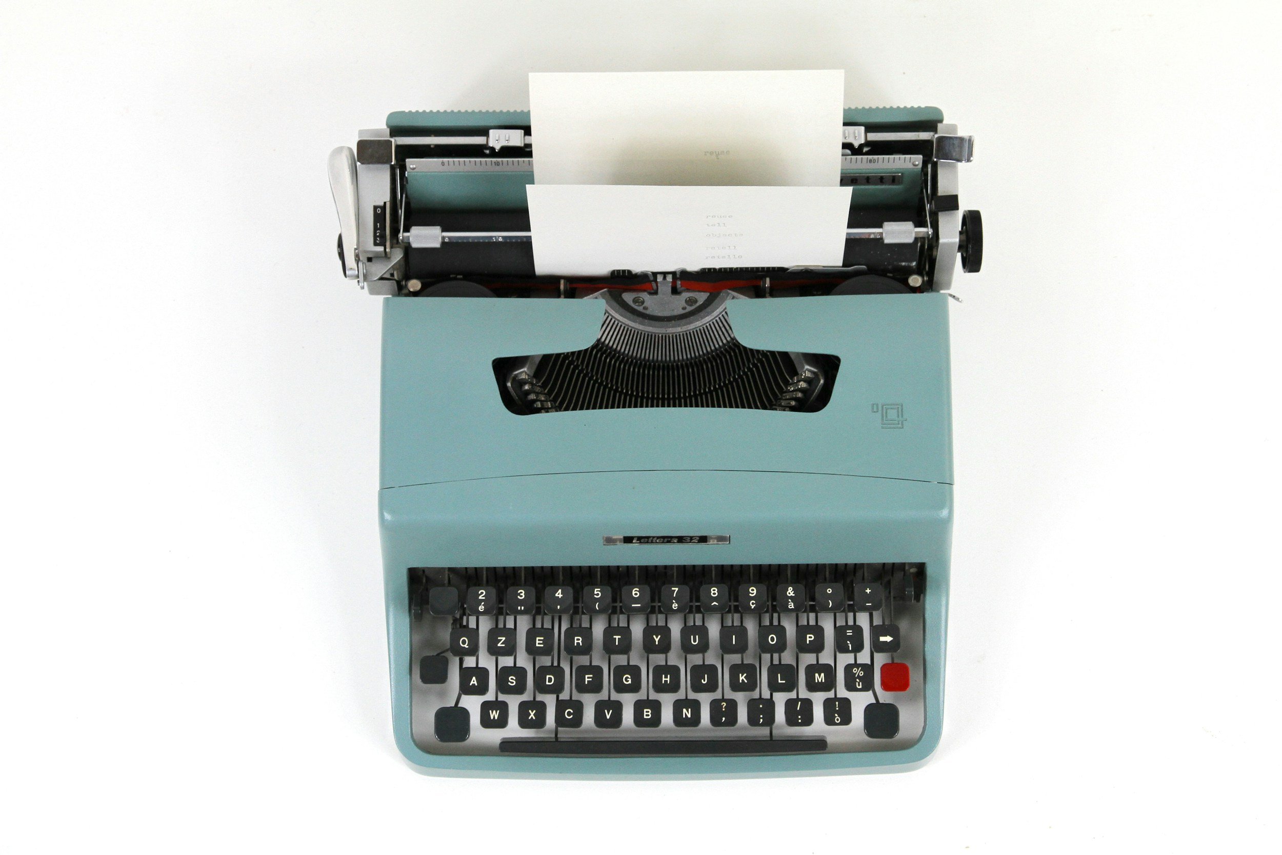 A vintage light blue typewriter with white papers inserted into the roller, seen from above on a white background.