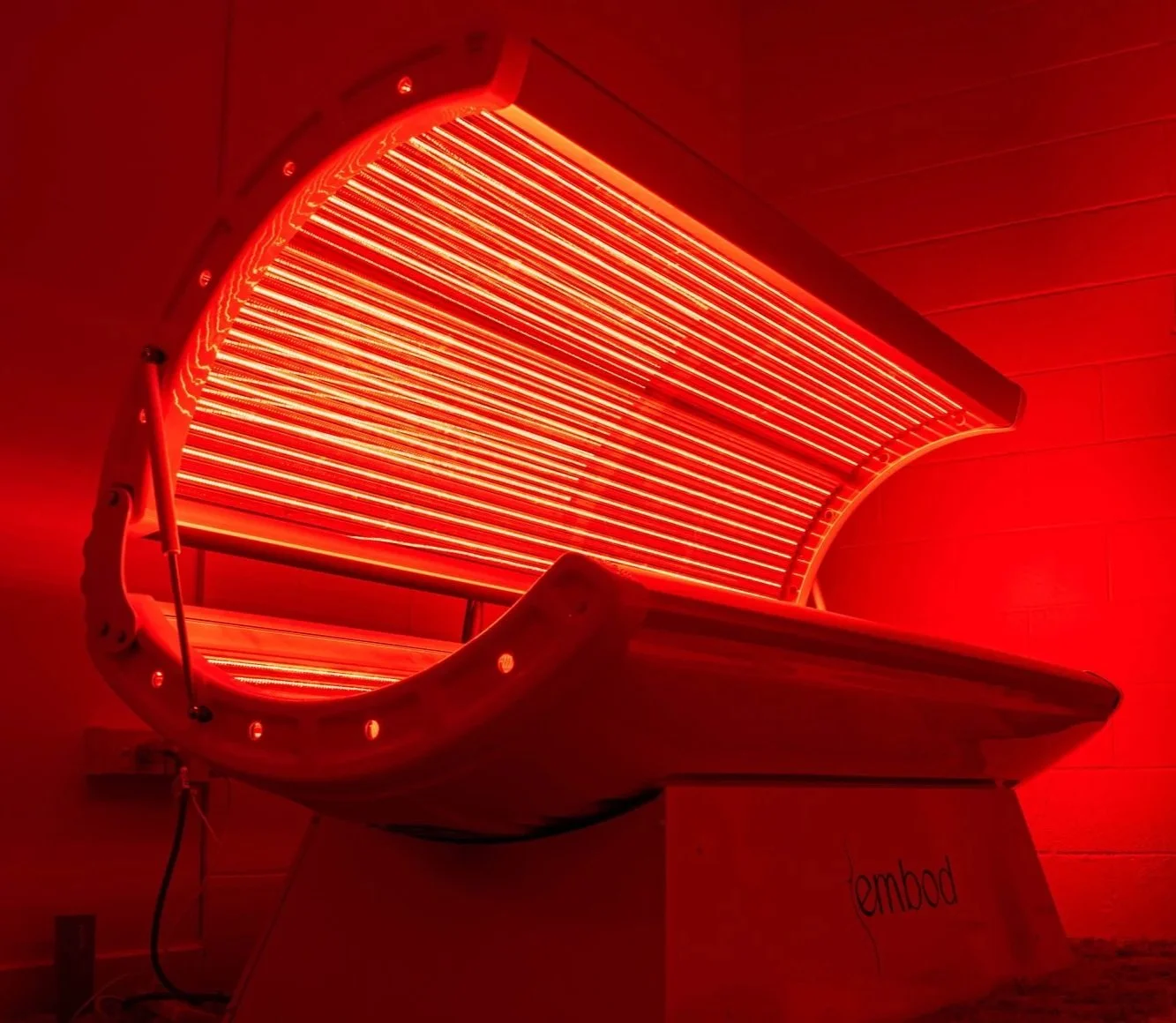 A red tanning bed with bright ultraviolet light tubes inside, turned on in a dimly lit room.
