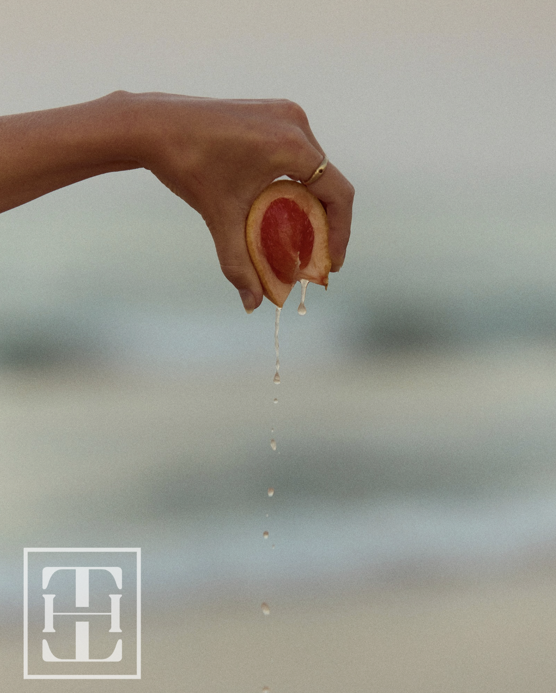 A hand holding a sliced peach with juice dripping down, against a neutral blurred background.