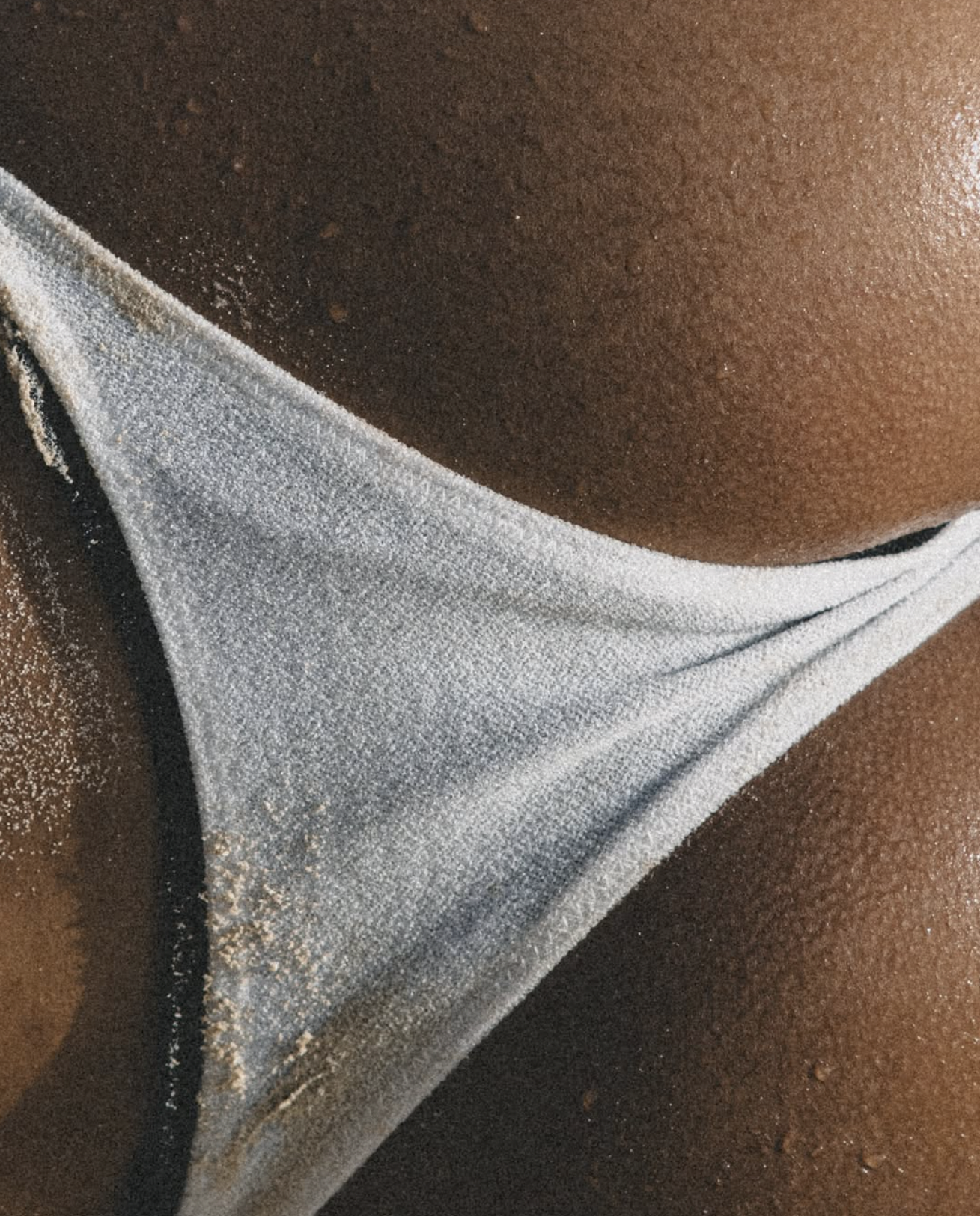 Close-up of a person's lower body in a white and black swimsuit lying on sandy beach.