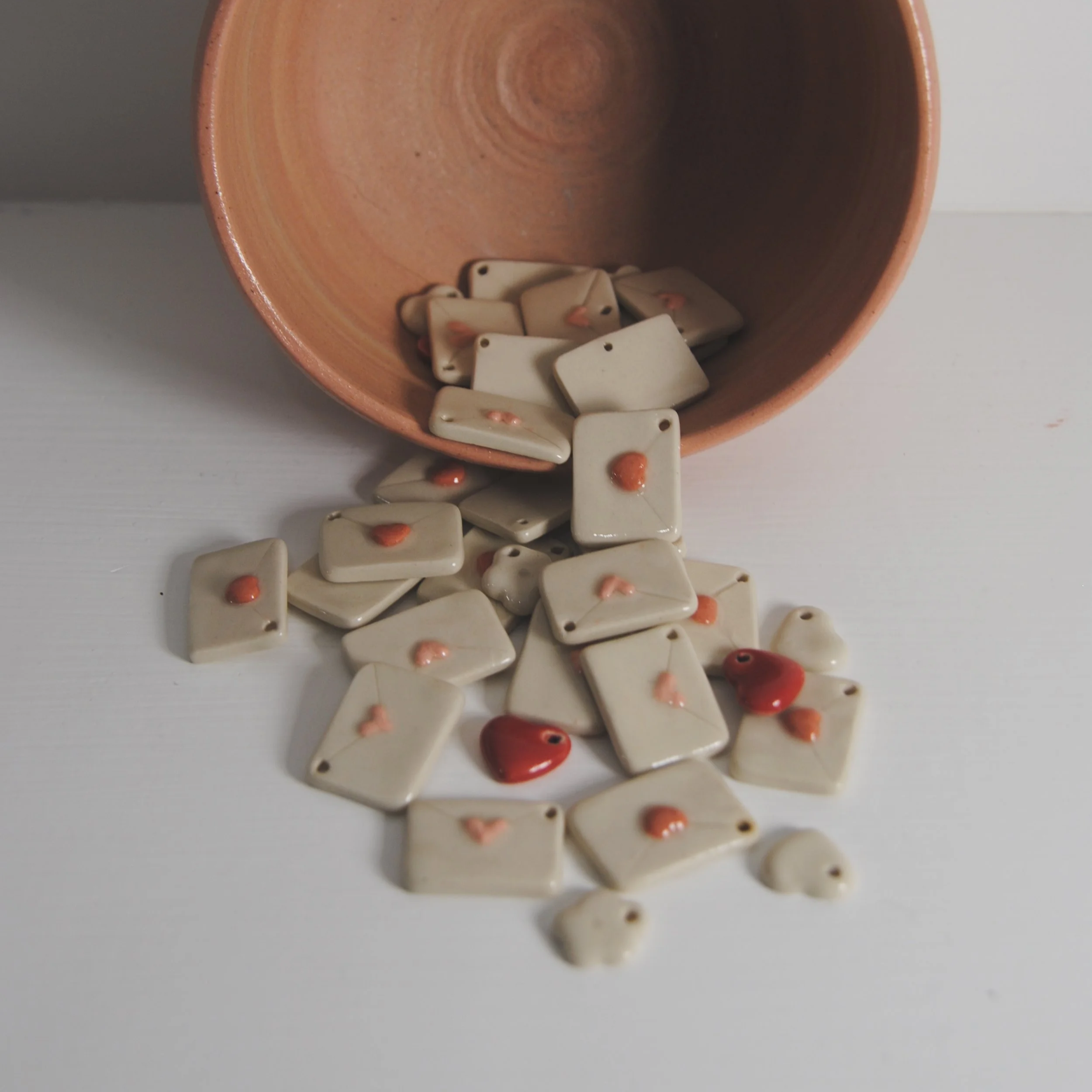 Ceramic tiles with heart-shaped designs spilling from a terracotta pot onto a white surface.