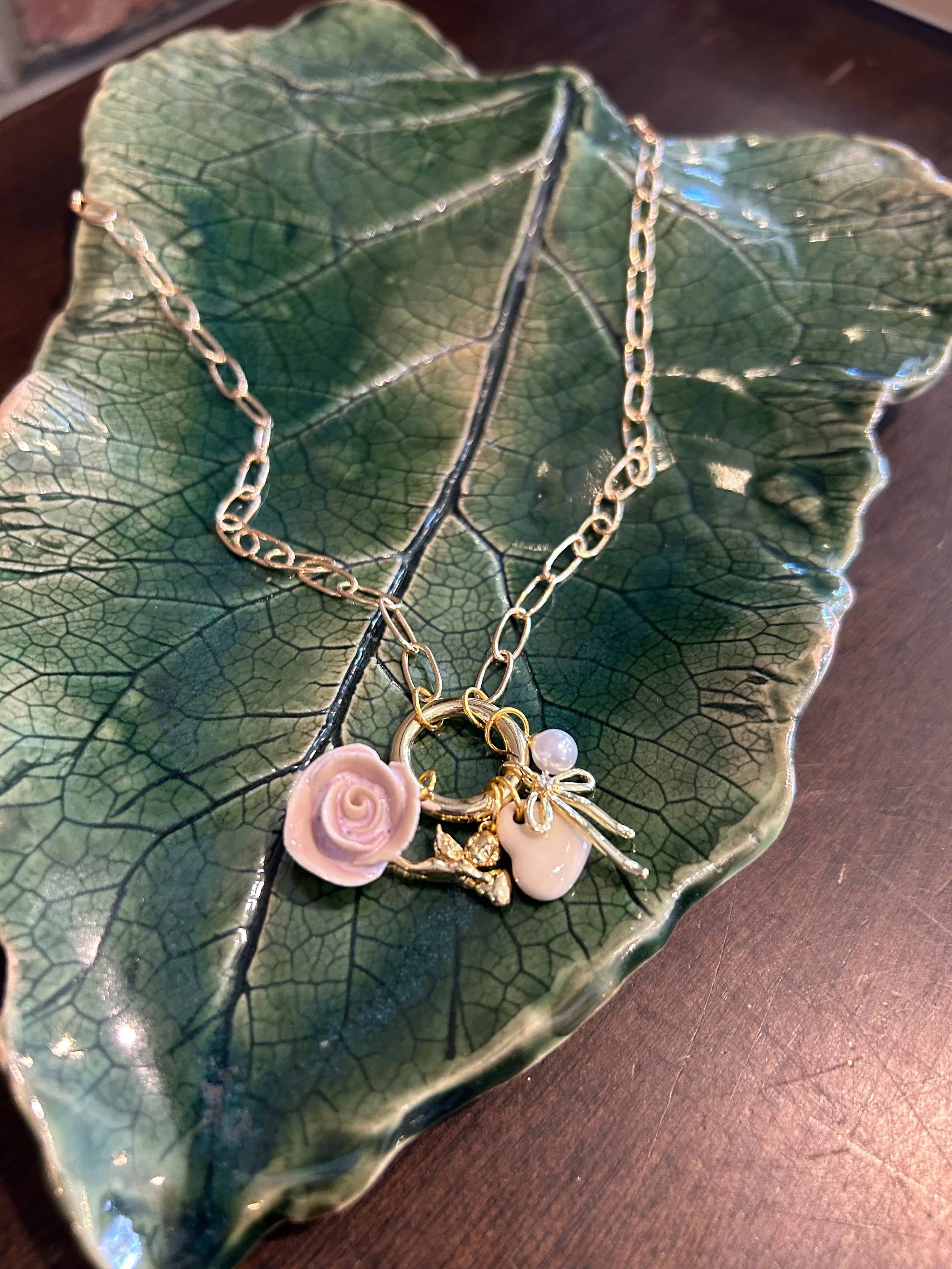 Gold chain necklace with flower, pearl, and leaf charms resting on a green leaf-shaped dish.