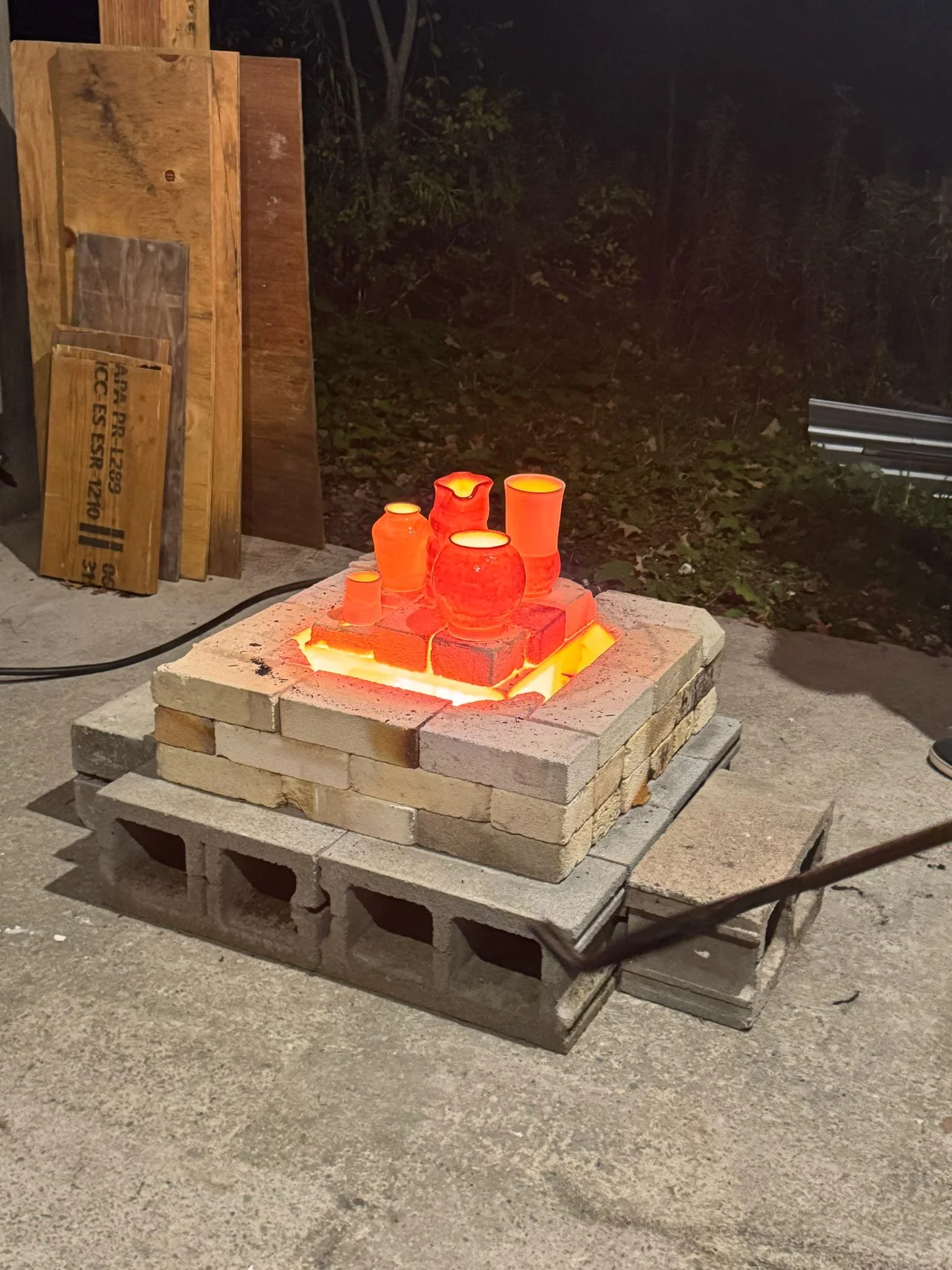 Upside-down glassware casting a red glow on bricks, placed on a cinder block fire pit in an outdoor setting at night.