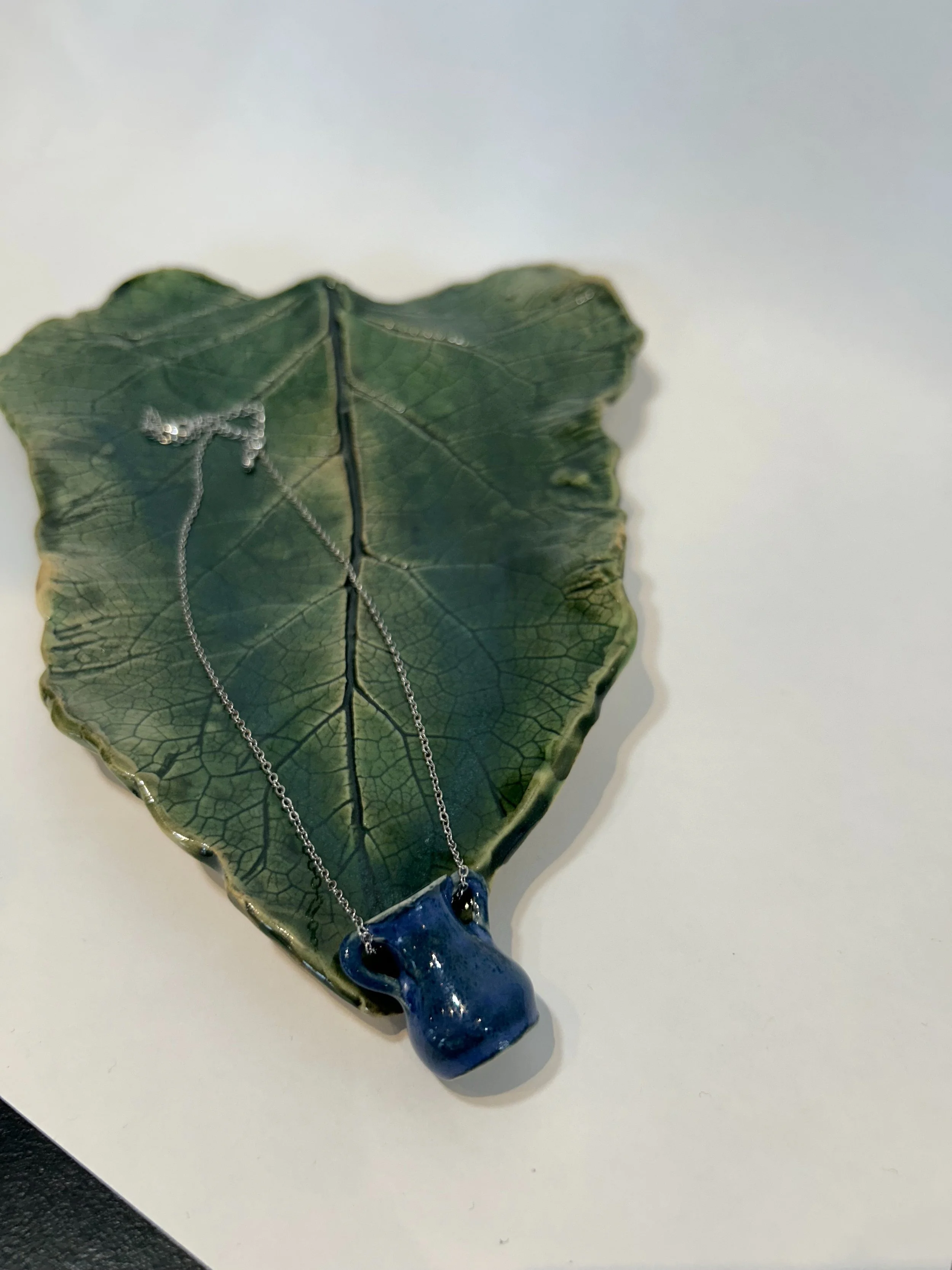 A blue glass necklace with a chunky pendant resting on a green leaf-shaped dish.