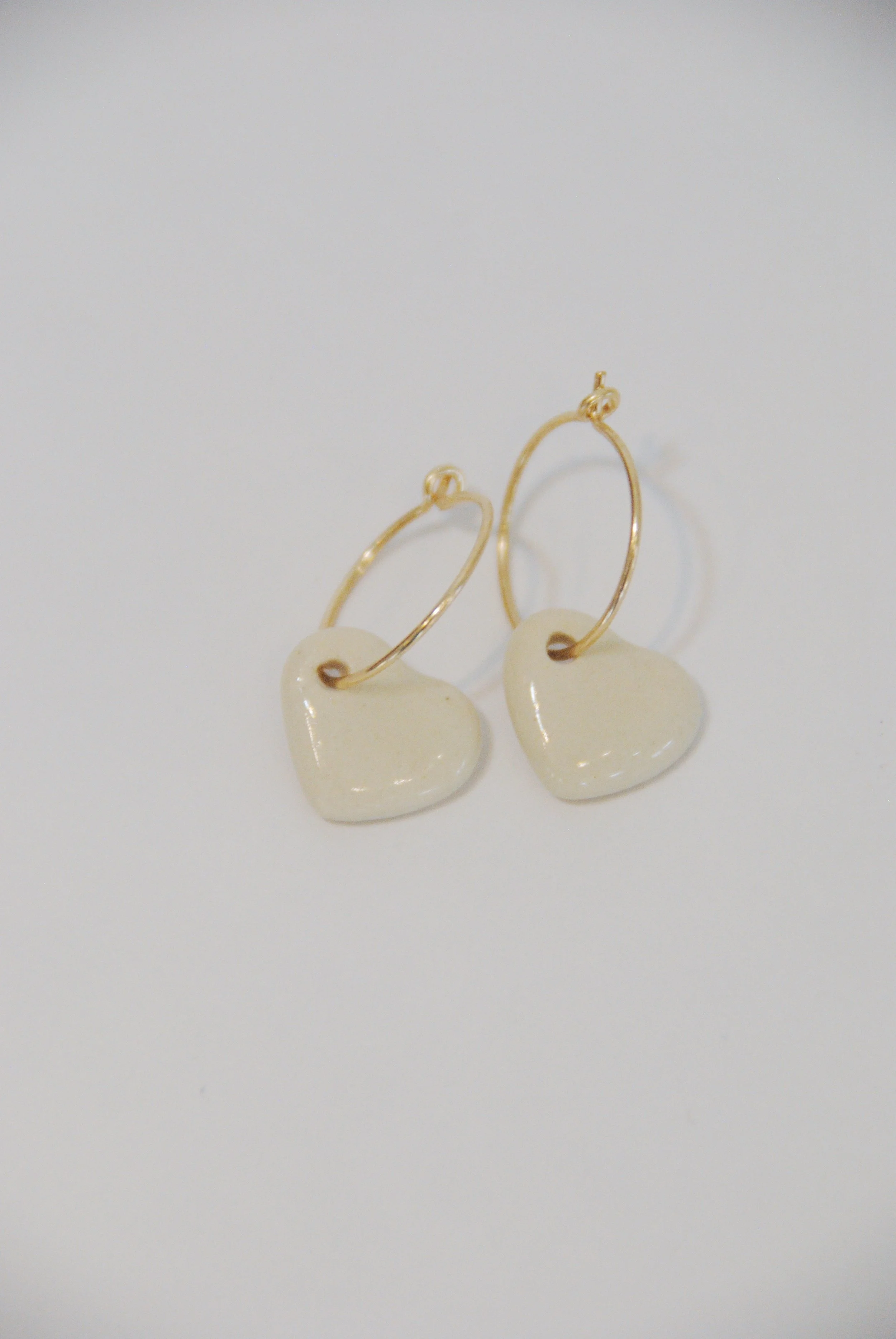 Gold hoop earrings with cream-colored heart-shaped pendants on a plain white background.