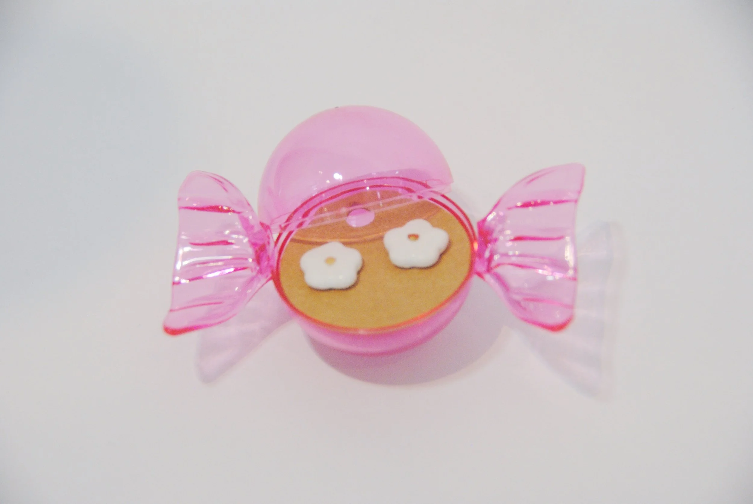 Pink plastic candy container shaped like a wrapped candy, with two small flower-shaped cookies inside.
