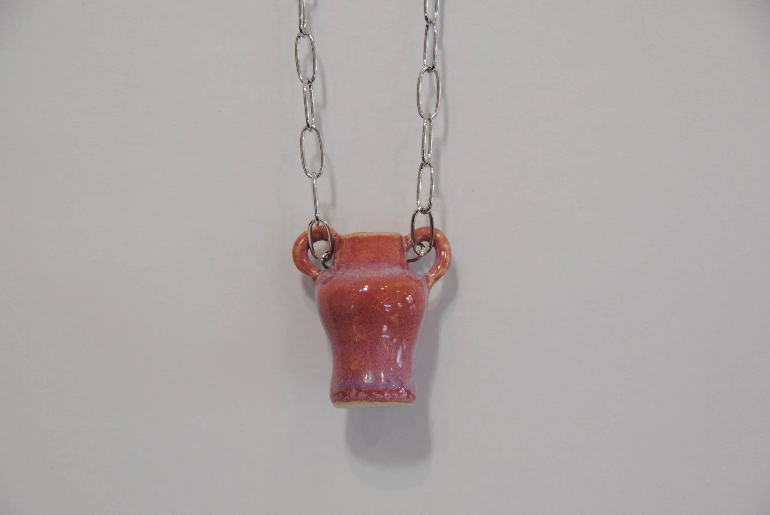 A necklace with a ceramic vase-shaped pendant hanging from a silver chain against a white background.