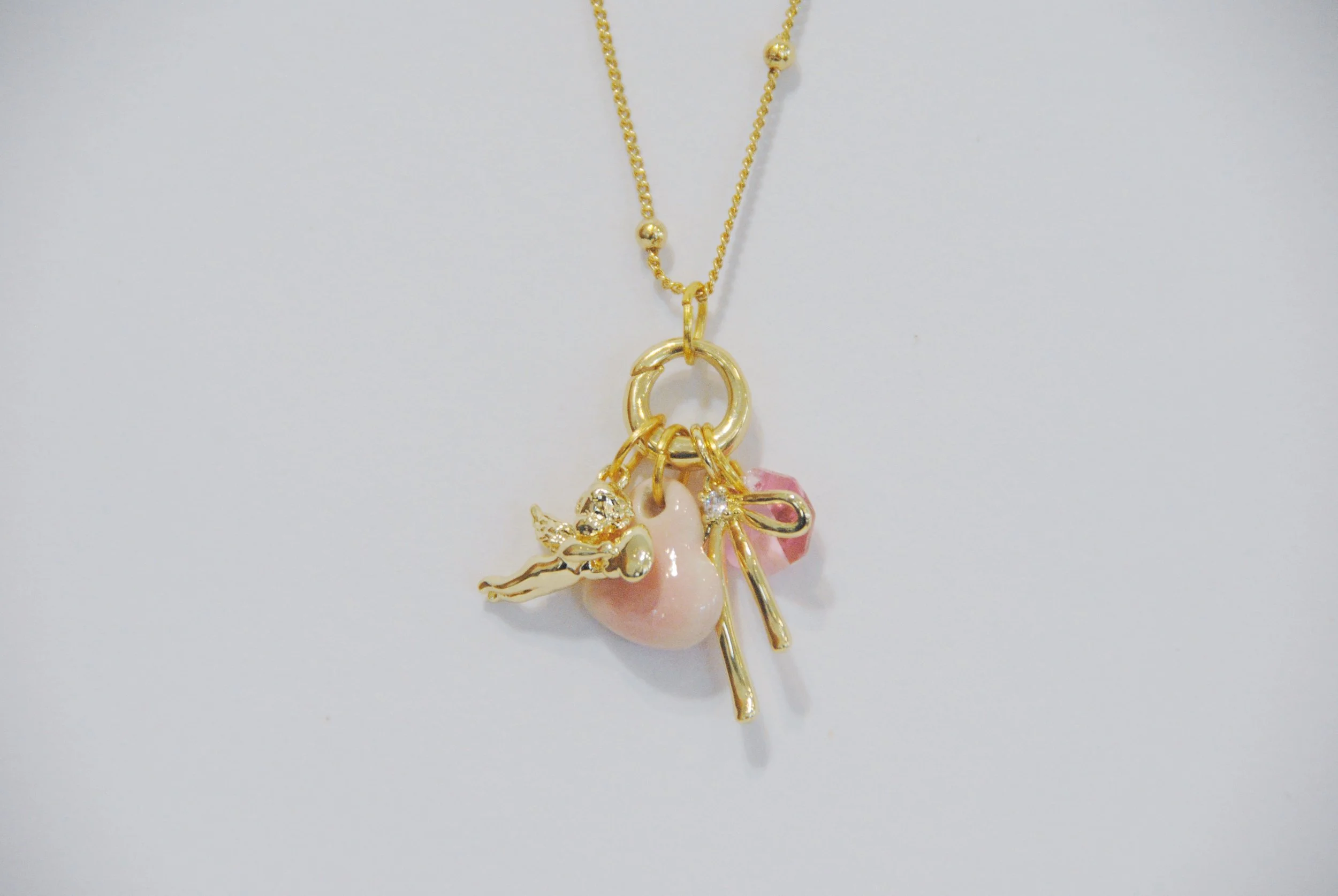 Gold necklace with charms including a pink pearl, a fairy, a key, and a pink rose.