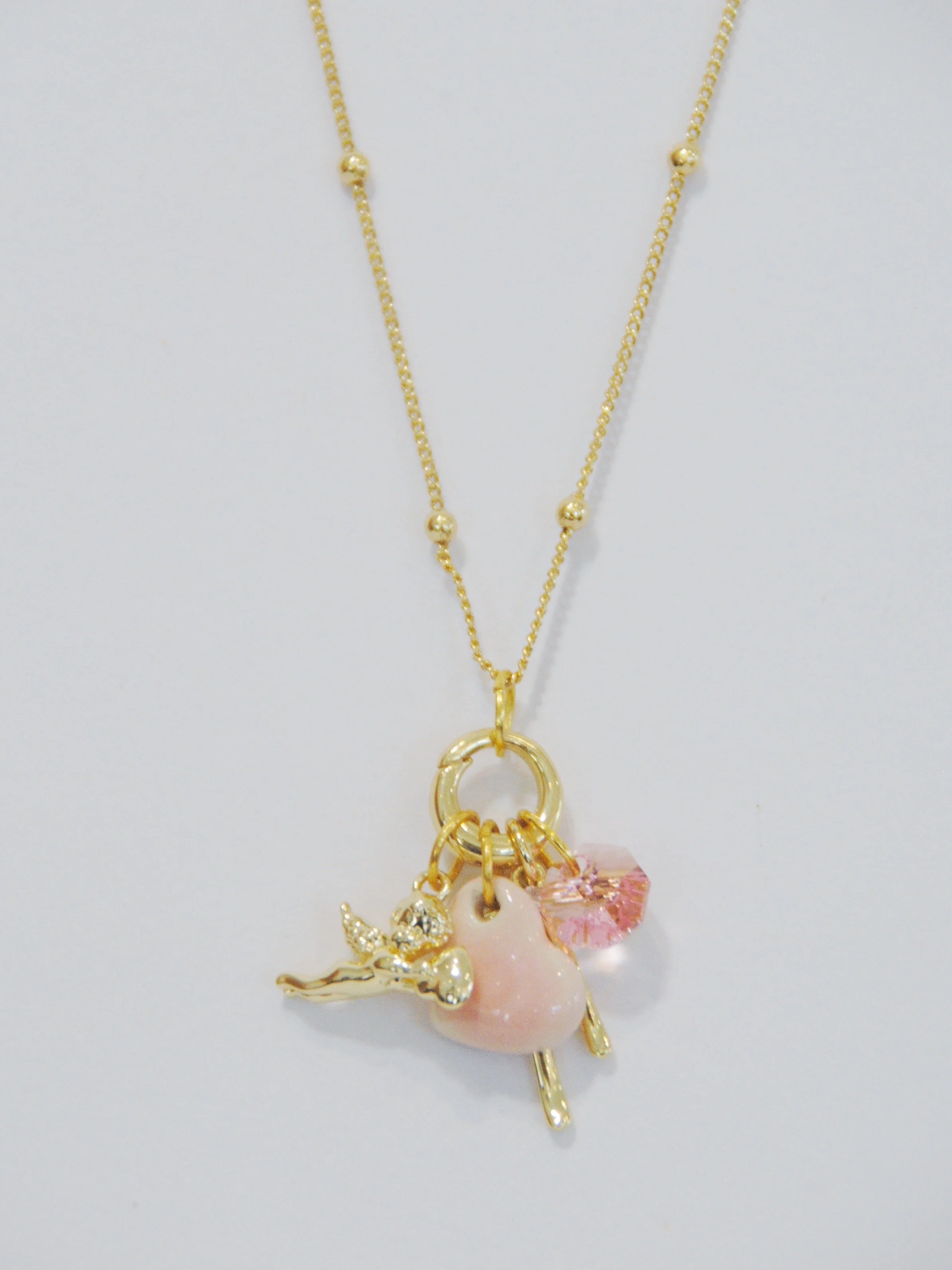 Gold necklace with ballerina charm, pink heart, and pink gemstone pendant.