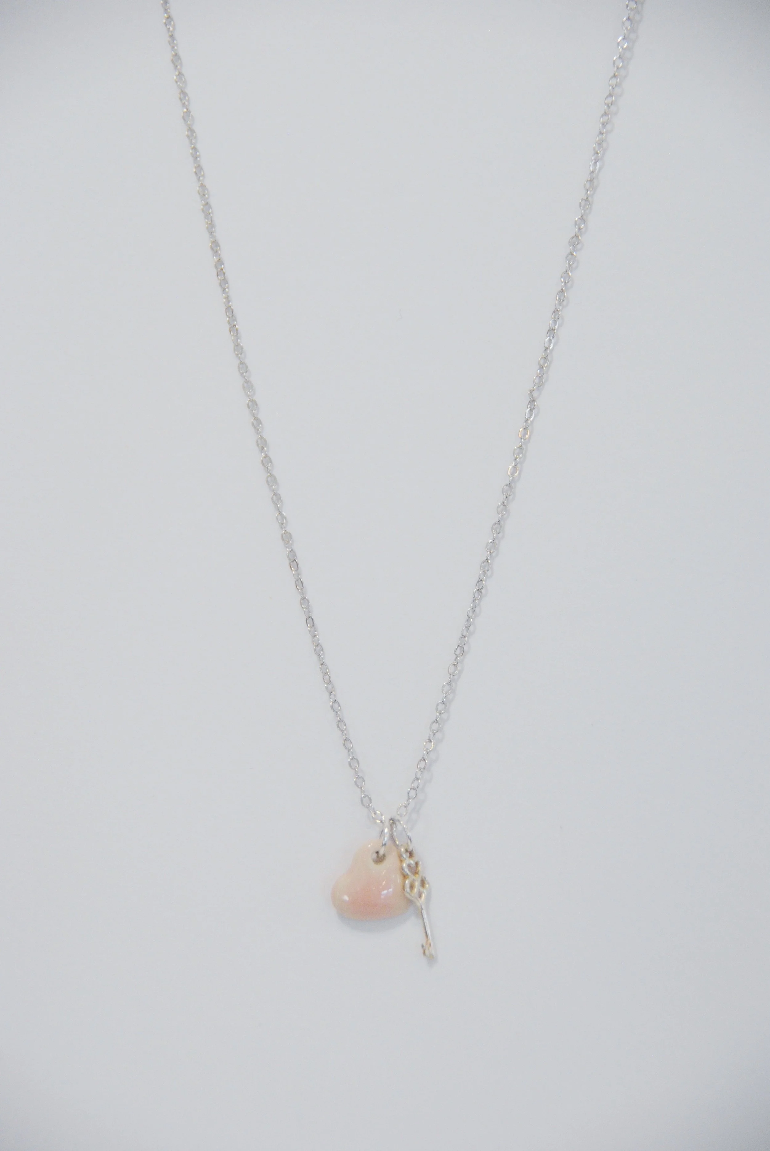 A silver chain necklace with a pink heart-shaped pendant and a small silver key charm.