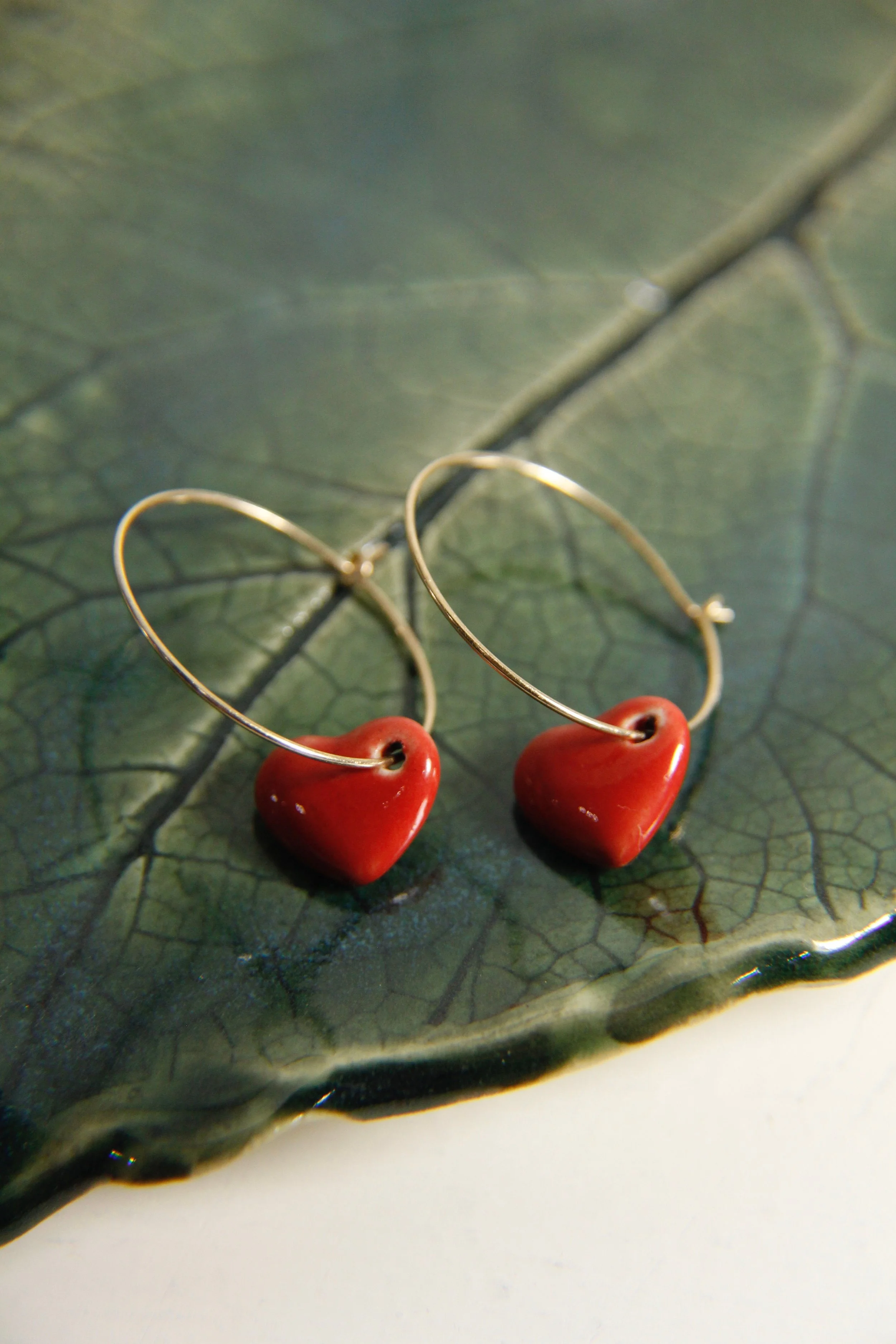 Stylish earrings with red heart-shaped beads on a dark green leaf.