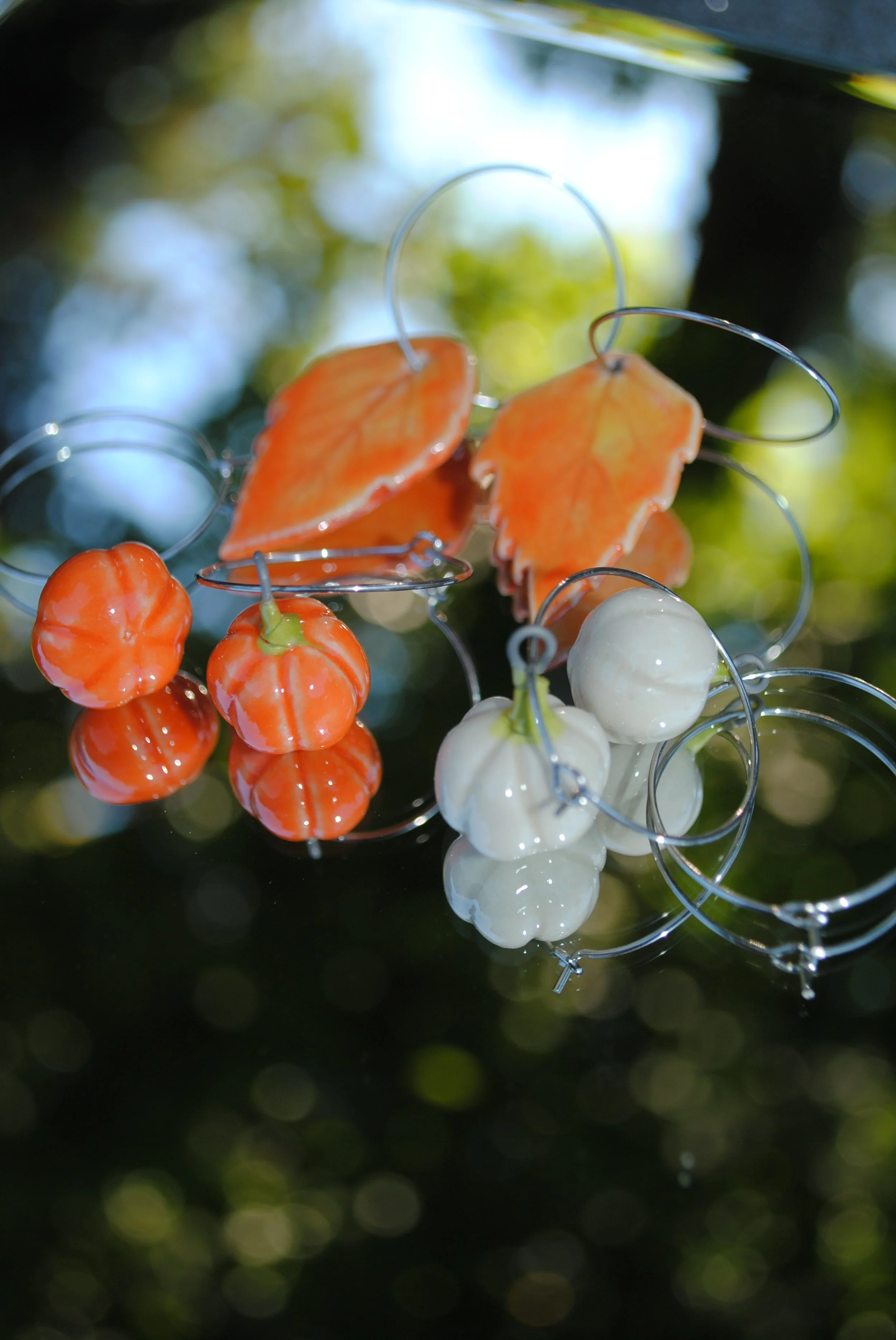 Decorative pumpkin-shaped ornaments and fall leaf ornaments hanging from silver wires outdoors.