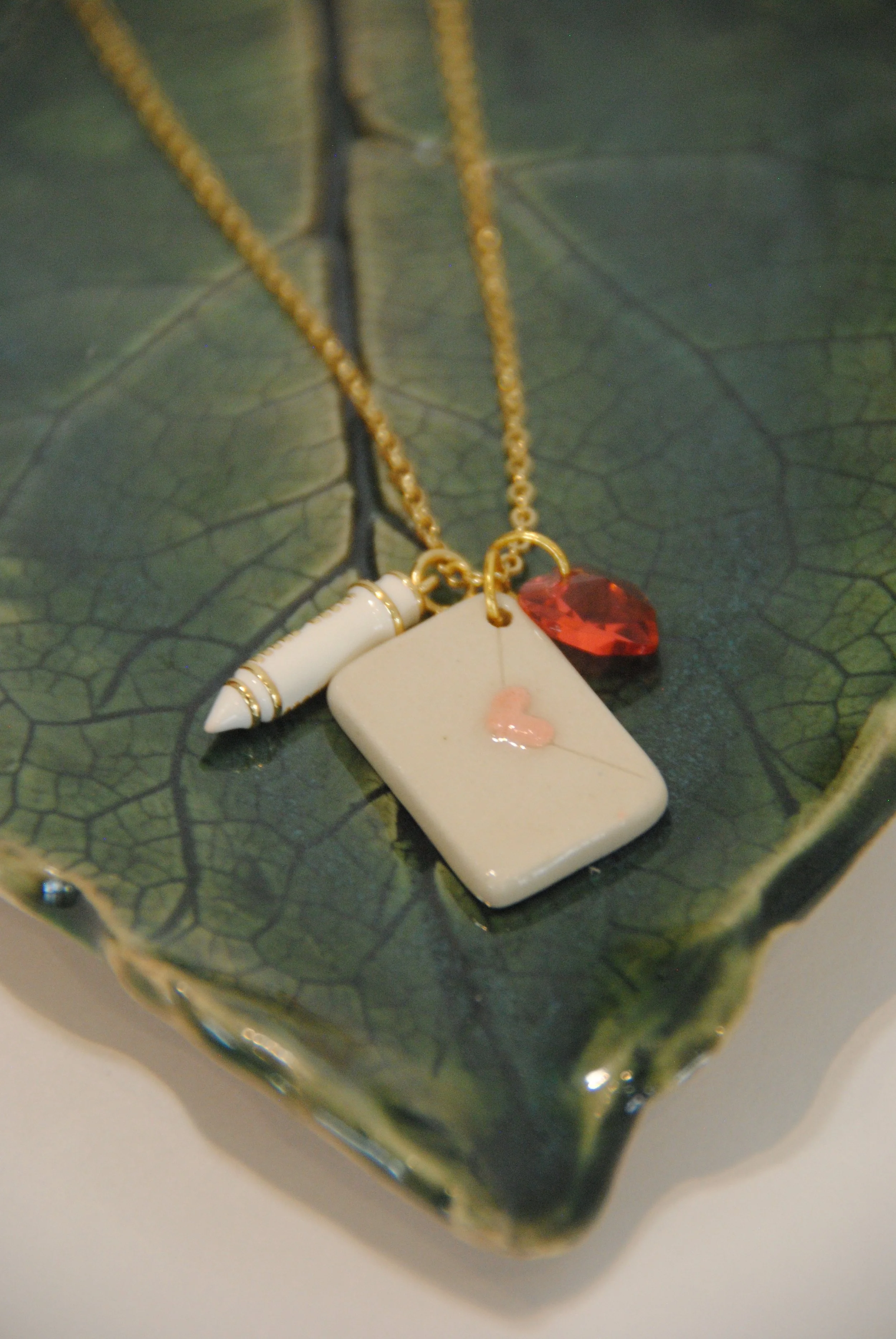 Necklace with a white pendant, a red gemstone, and a white and gold charm on a green leaf-shaped dish.