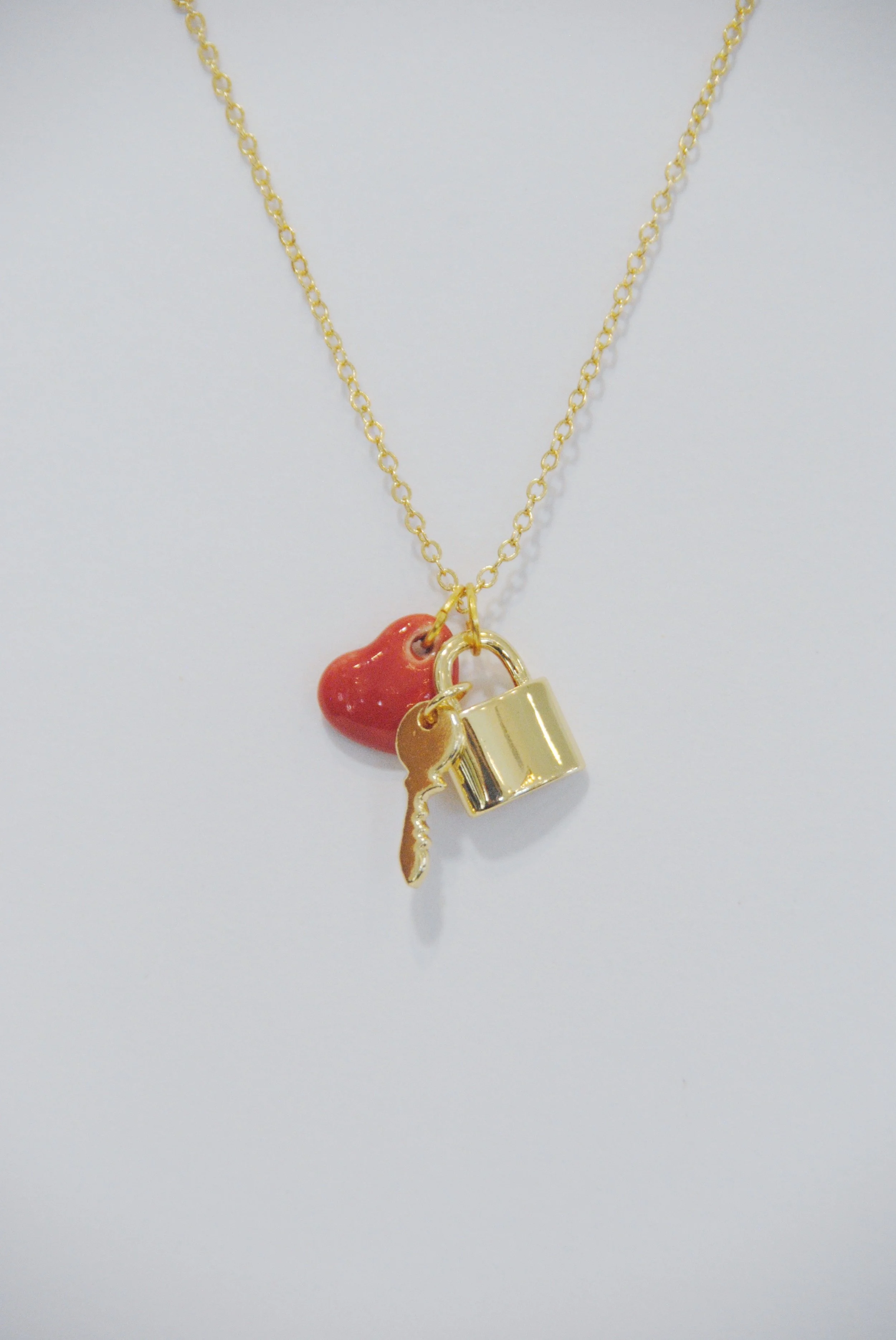 Gold necklace with three charms: a red heart, a gold key, and a gold padlock