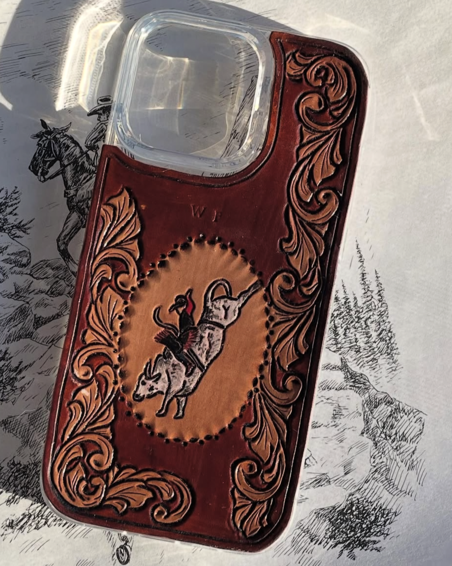 A shot glass with a leather holder featuring a cowboy riding a bucking bull, embroidered and decorated with ornate scrollwork.