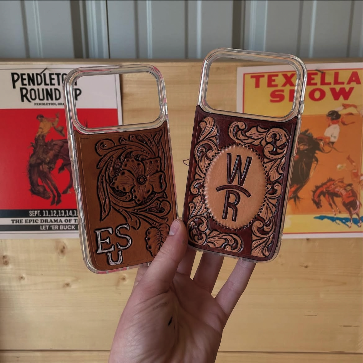 Two decorative leather phone wallets with floral and ornate designs, each marked with initials: E, S, U on one and W, R on the other, held in front of rodeo event posters.