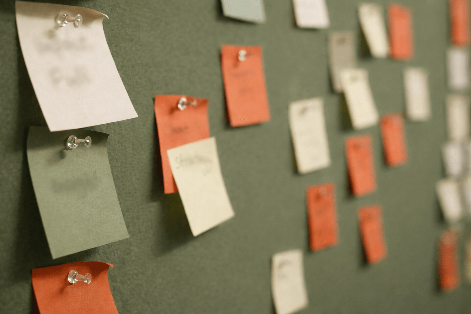 green noticeboard with orange and cream handwritten post it notes pinned