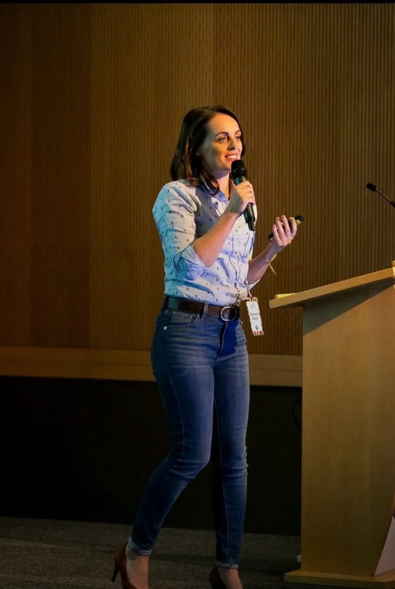 Rowena Doyle speaking at a conference with microphone and podium.