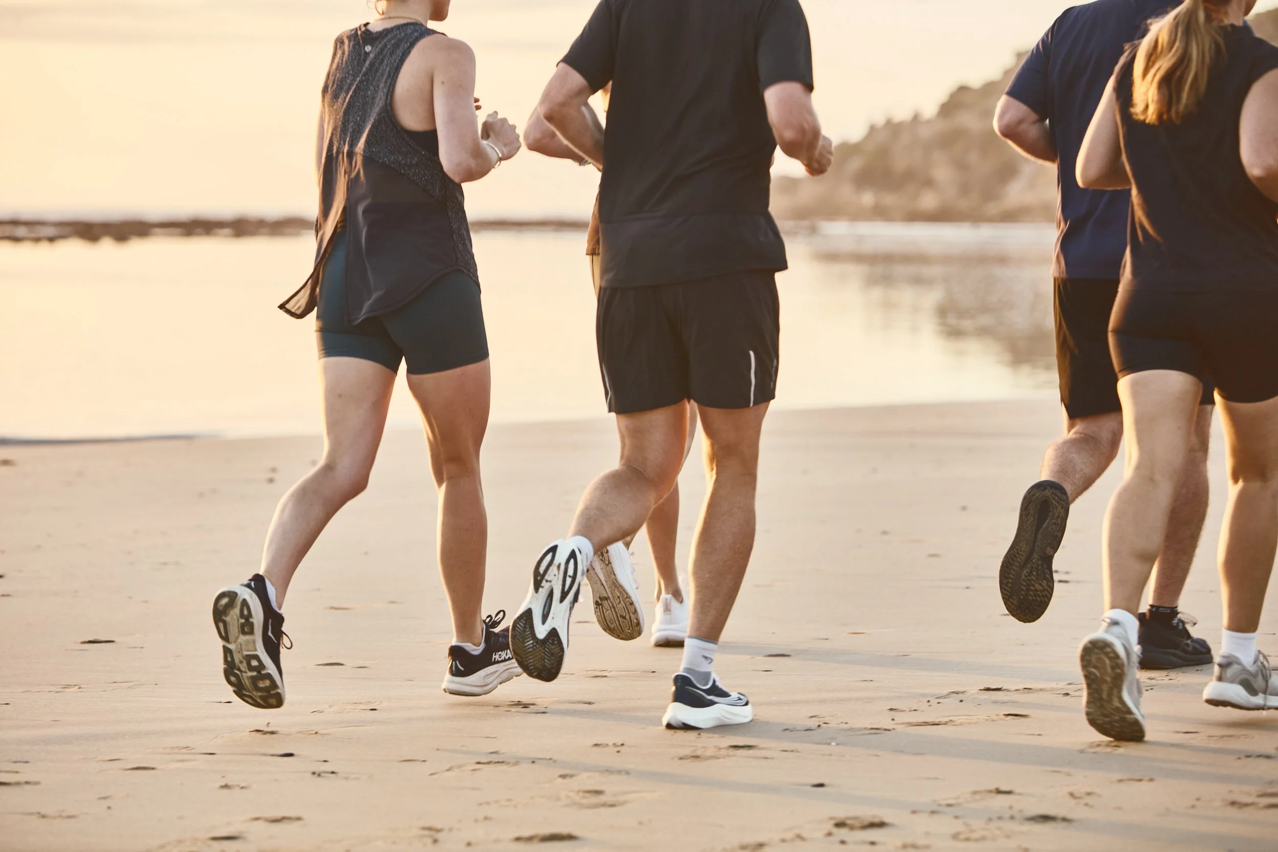 A group of people jogging on the beach at sunset.