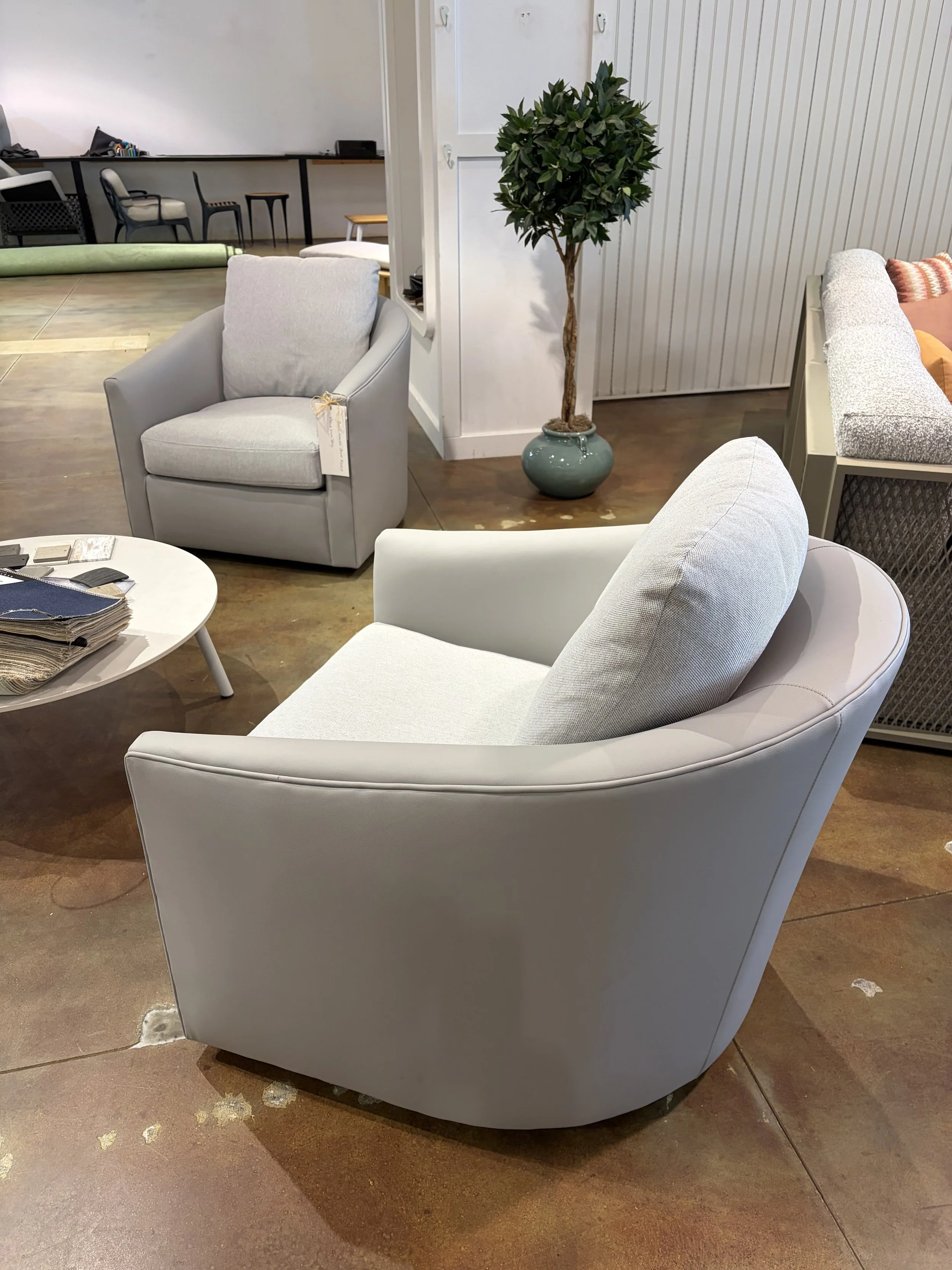 White modern armchair in a furniture store, with a cushion, sitting on a hardwood floor.