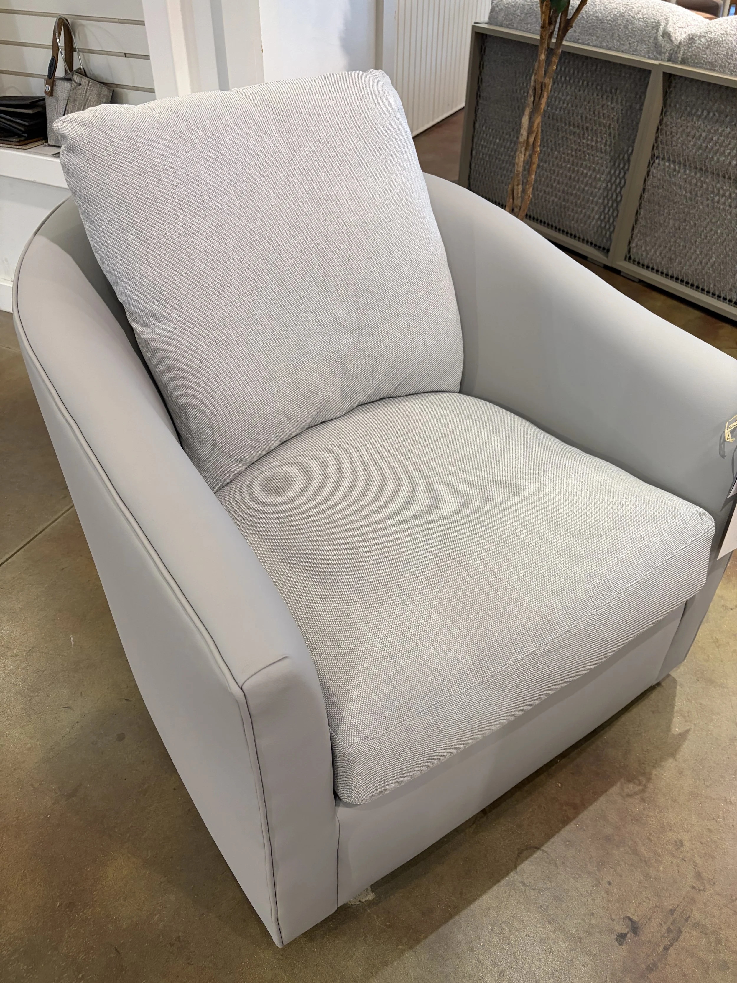 A modern armchair with light gray fabric cushions and a sturdy gray frame, situated on a concrete floor in a furniture store.