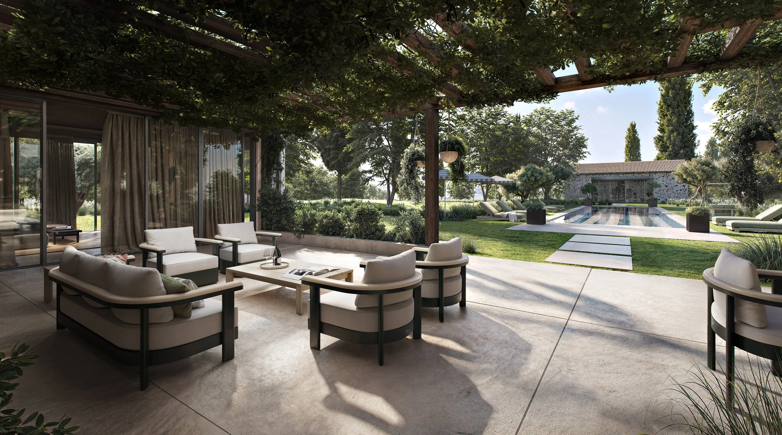 Outdoor patio area with white cushioned chairs and a table, overlooking a backyard with a swimming pool, lounge chairs, lush trees, and a stone building in the background.