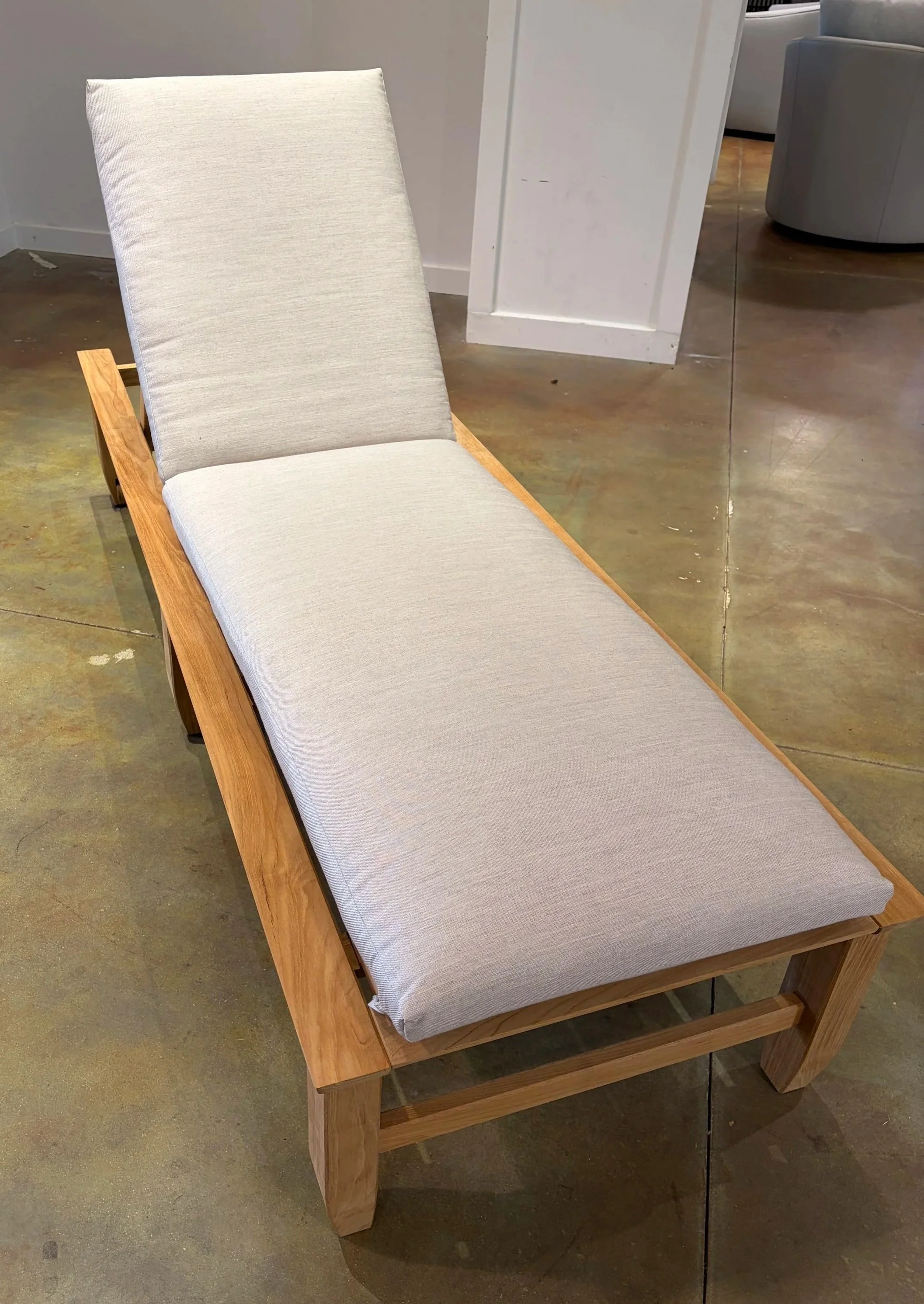 A wooden bench with a light gray cushion on top, situated on a concrete floor in a furniture store.