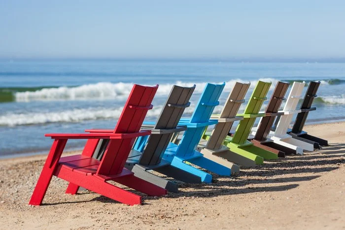 Colorful Adirondack chairs on sandy beach near ocean waves under clear sky.