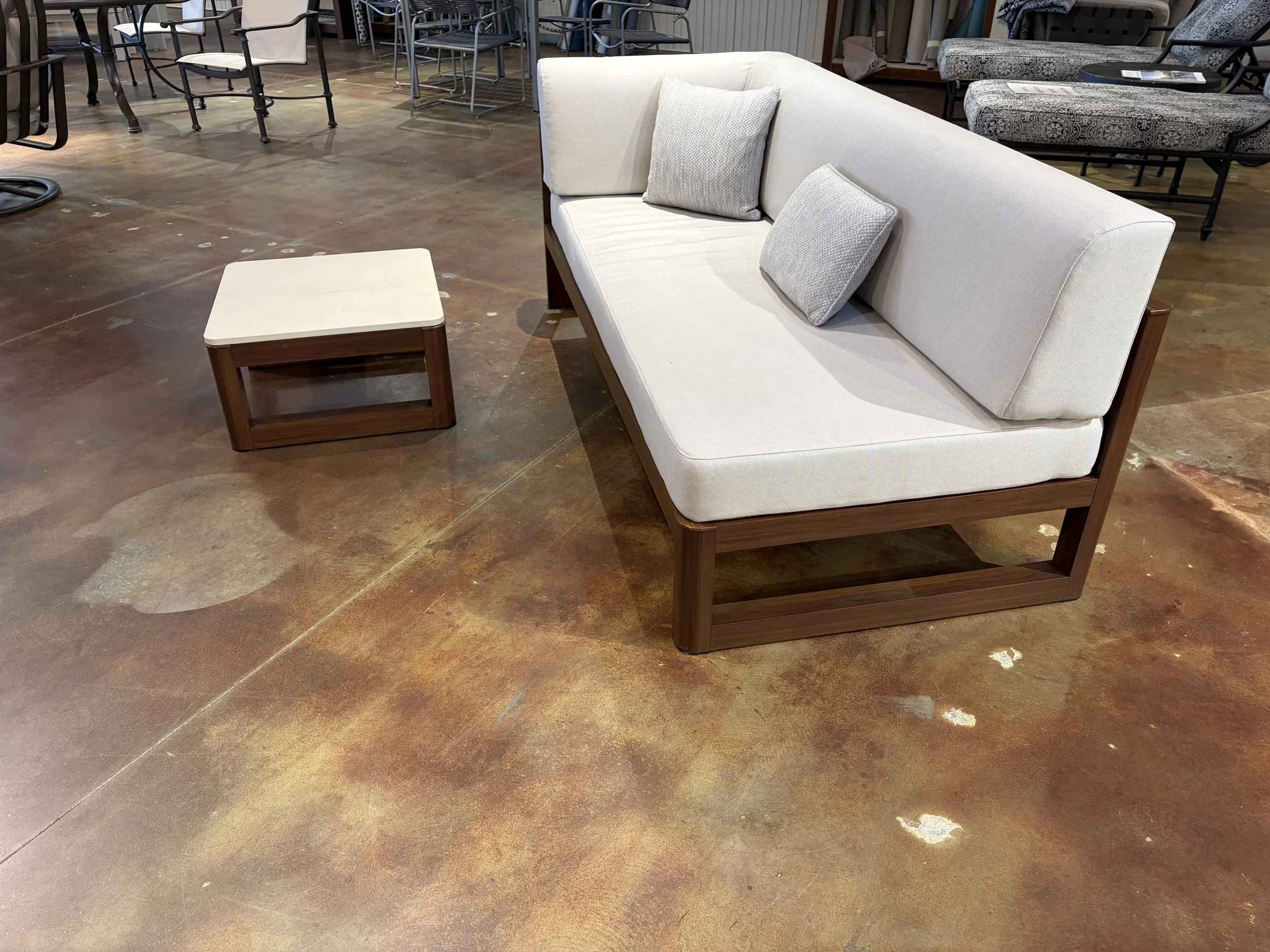 A furniture display with a beige sofa, two decorative pillows, a side table, and various chairs in the background.