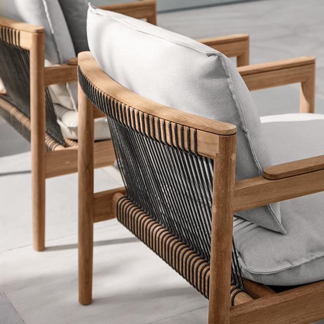 Close-up of a wooden-framed outdoor chair with gray cushions and black rope detail on the backrest. Gloster