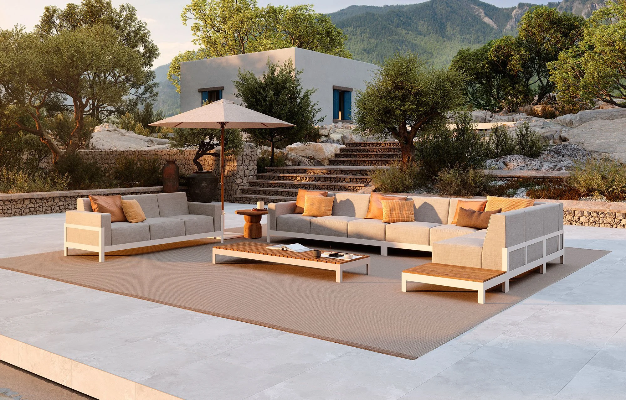 Modern outdoor patio with beige sectional sofa and pillows, wooden coffee table, large umbrella, surrounded by trees, rocky landscape, white house with blue shutters, mountain in the background during sunset.