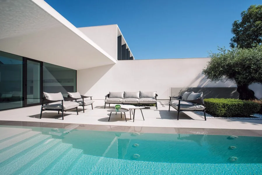 Modern outdoor patio with lounge chairs and a swimming pool under a clear blue sky.