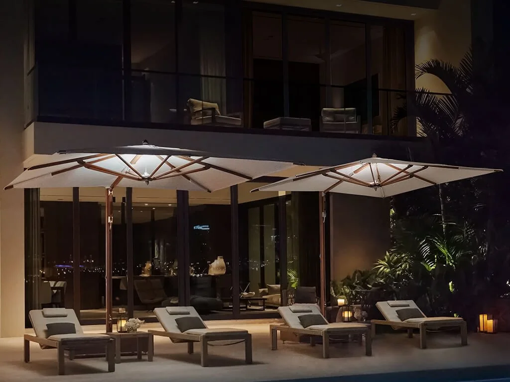Outdoor patio with four lounge chairs, two large umbrellas, and ambient lighting at night. TUUCI Umbrellas