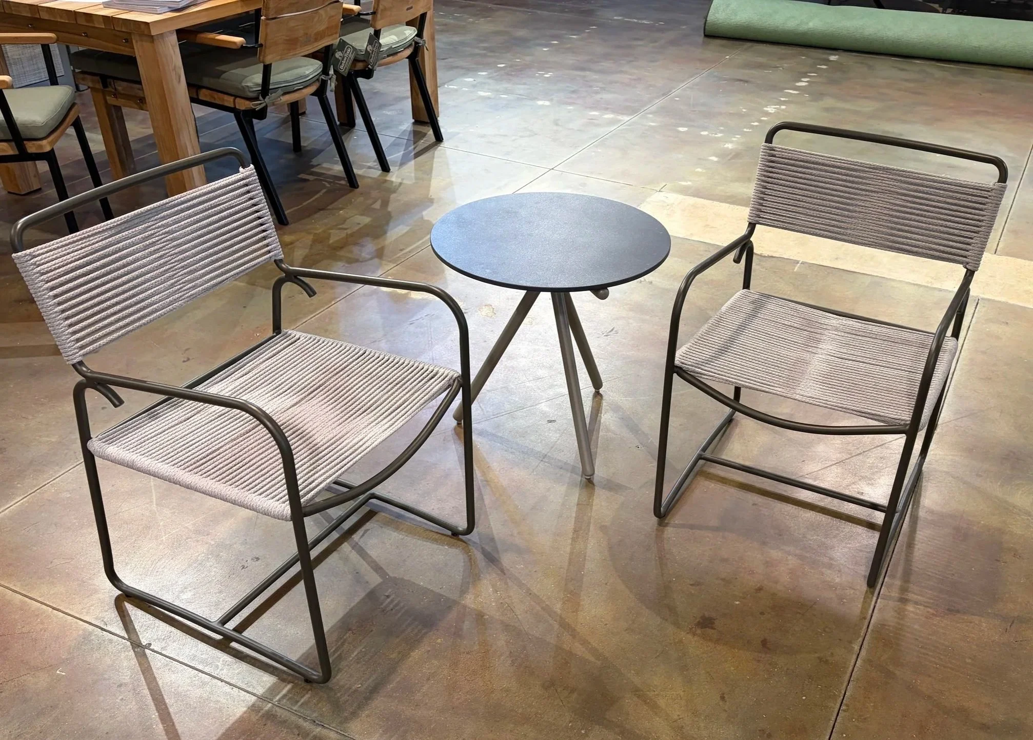 Two metal chairs with rope seats and backs placed around a small round table in a store or cafe setting.