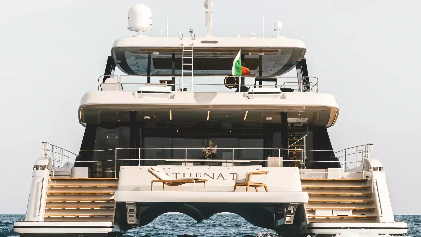 Luxury yacht with white exterior, multiple decks, and outdoor lounge area, sailing on the ocean under a clear sky, with an Italian flag on the top deck.
