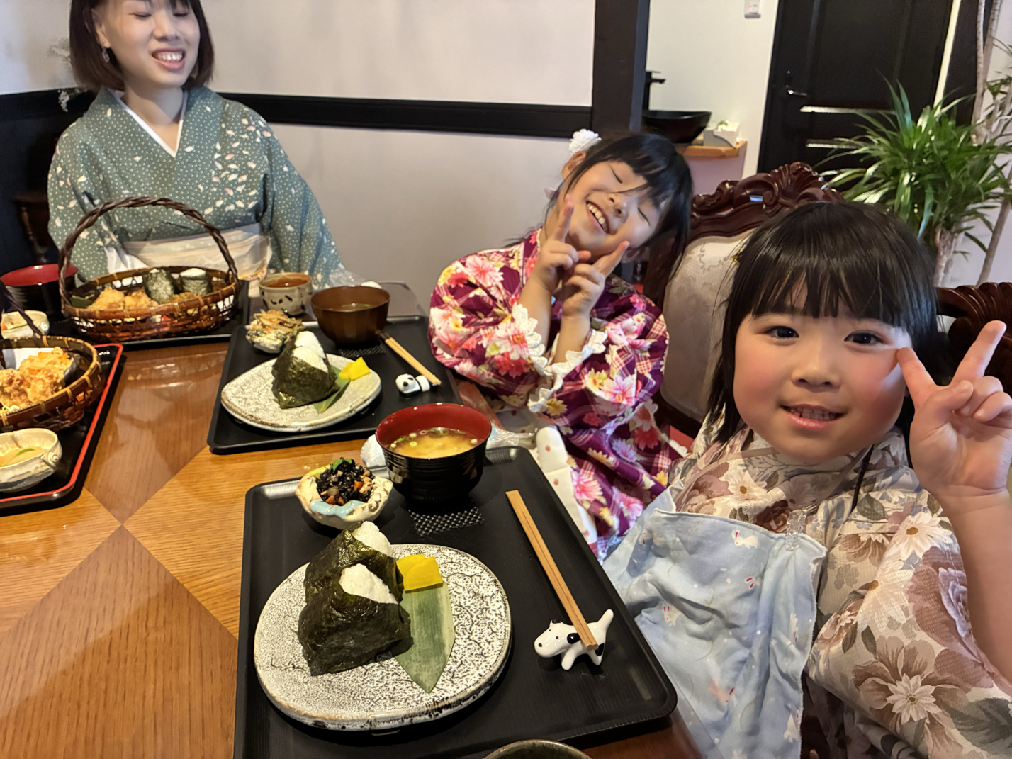 和室で座る女性と子供たちが着物を着て、和風の料理を楽しんでいる。子供たちはVサインをして笑っている。
