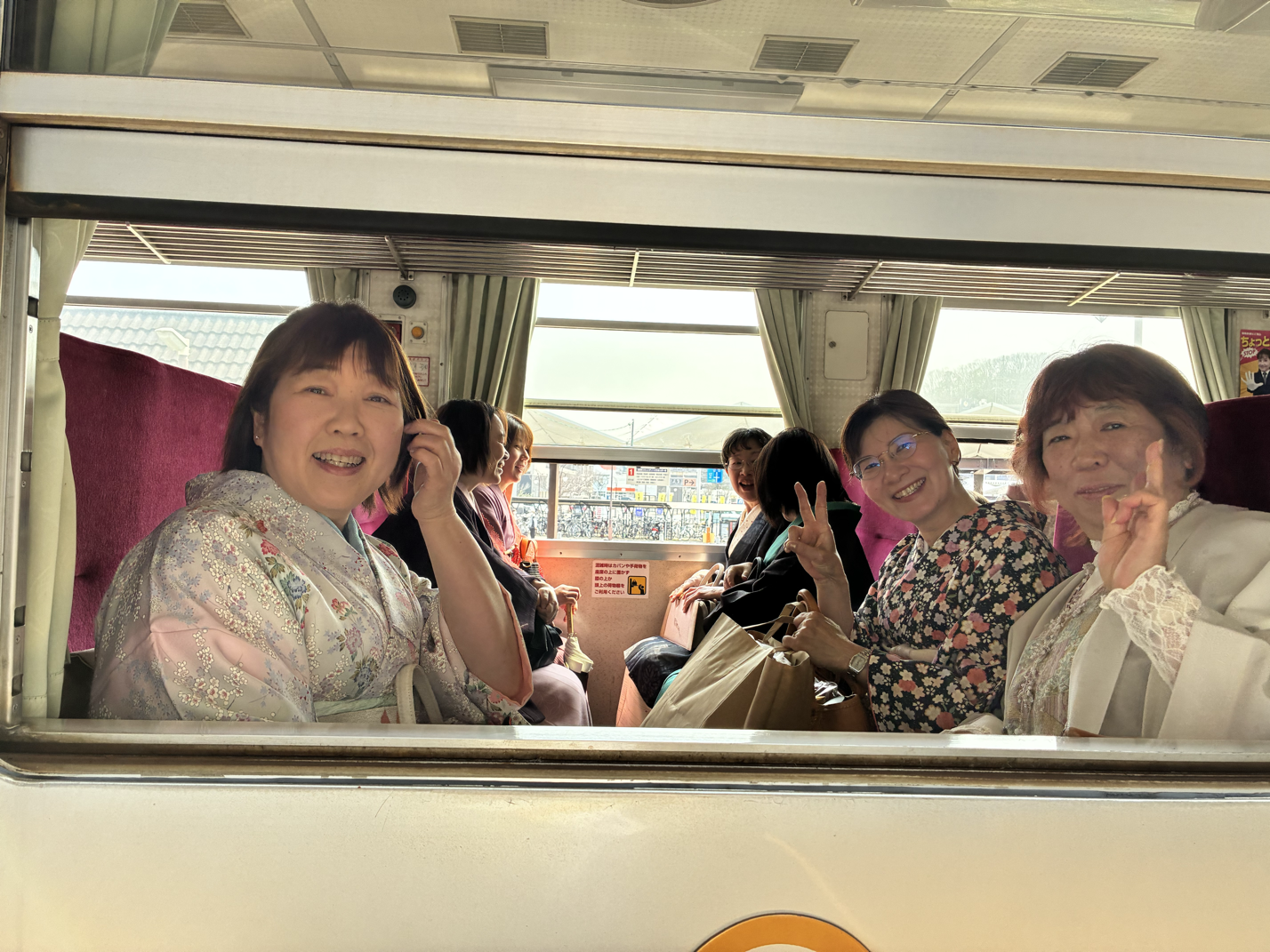 列車の窓側の座席に座るグループの女性たちが笑顔で写真に写っている。
