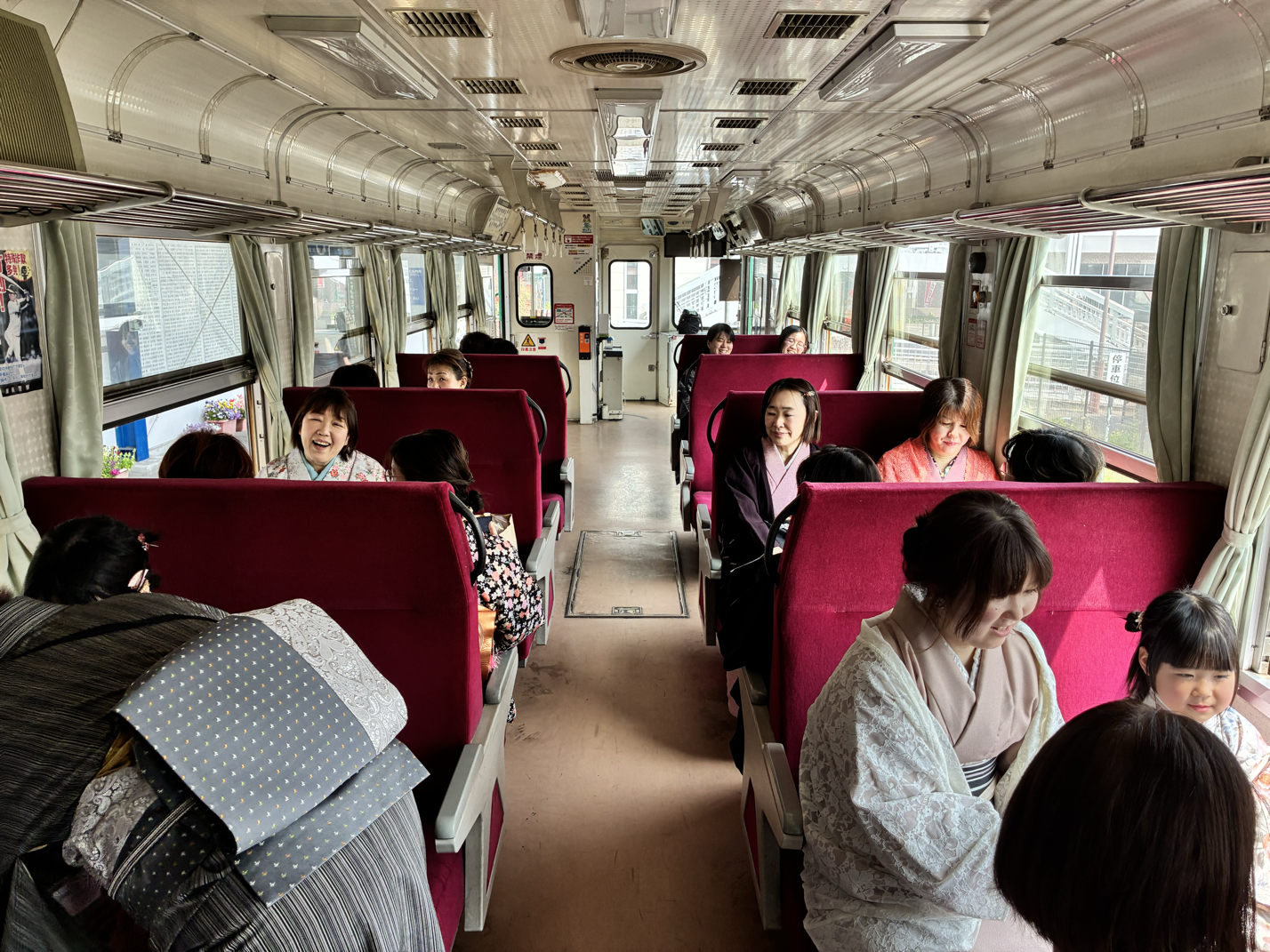 電車の車内に座る日本人女性と子供たち。窓の外に都市の景色が見える。
