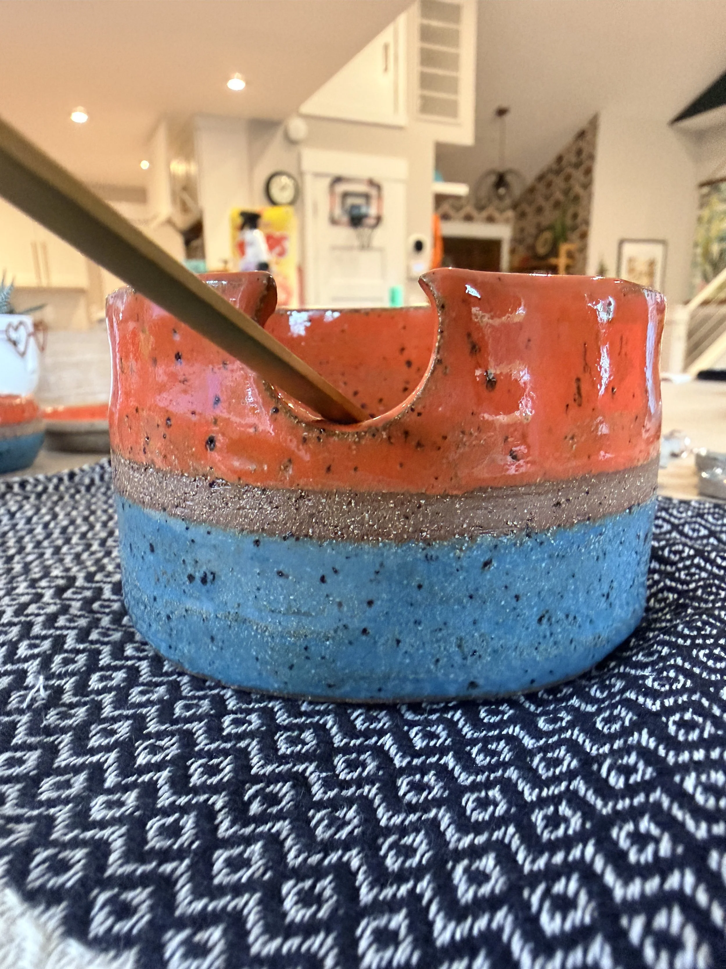 Close-up of a two-tone ceramic bowl with a small gold spoon resting inside, placed on a patterned tablecloth in a brightly decorated room.