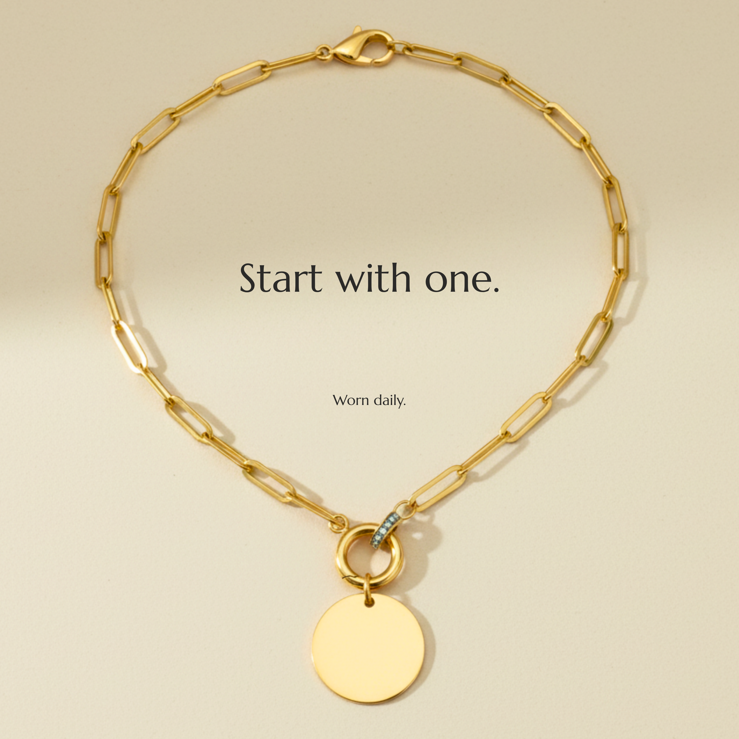 Gold chain necklace with a round pendant, displayed on a light-colored background with the text 'Start with one. Worn daily.'