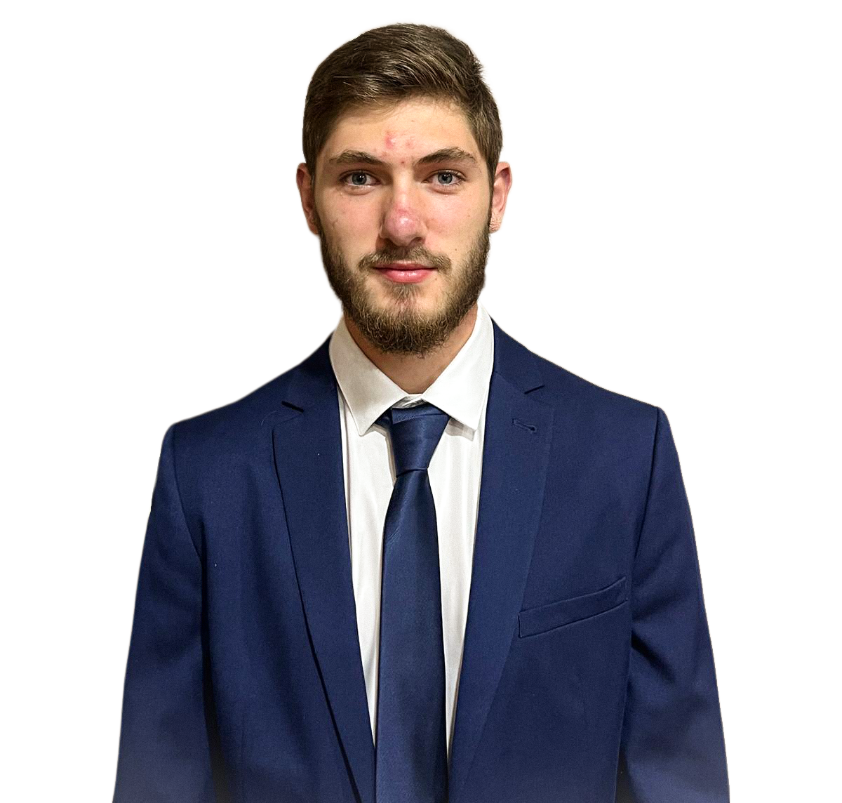 A young man with brown hair, beard, and light skin, dressed in a navy blue suit, white shirt, and navy blue tie, standing against a background with black and beige sections.