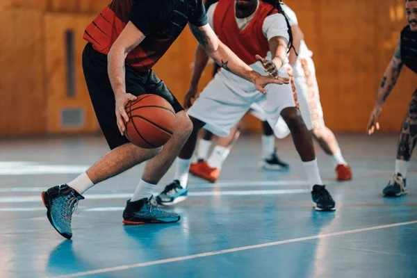 A group of young people playing basketball on an indoor court, with one player holding the basketball while others defend.