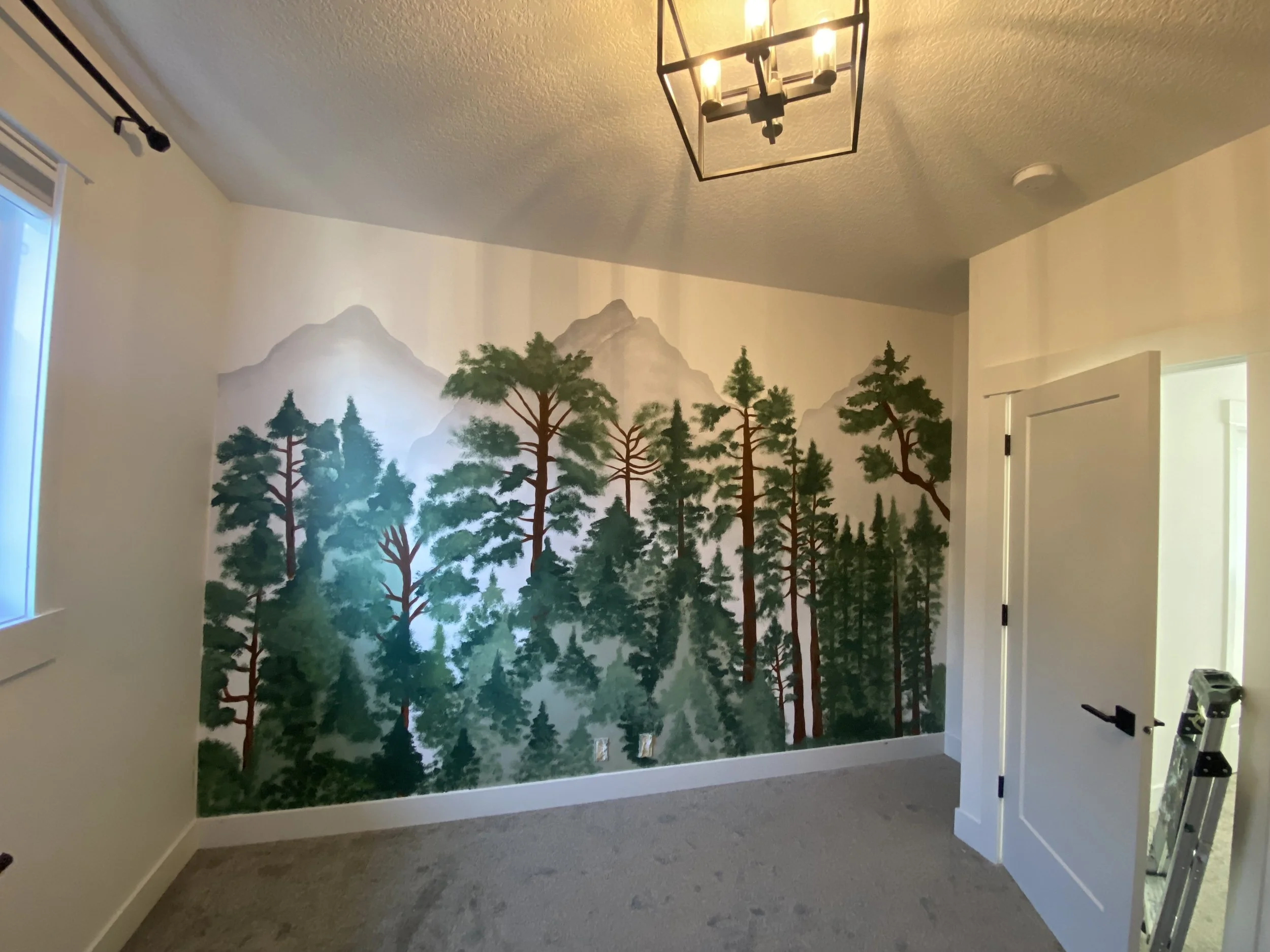 Interior of a room with a mountain and forest mural on the wall, a chandelier light fixture on the ceiling, and partially open door.