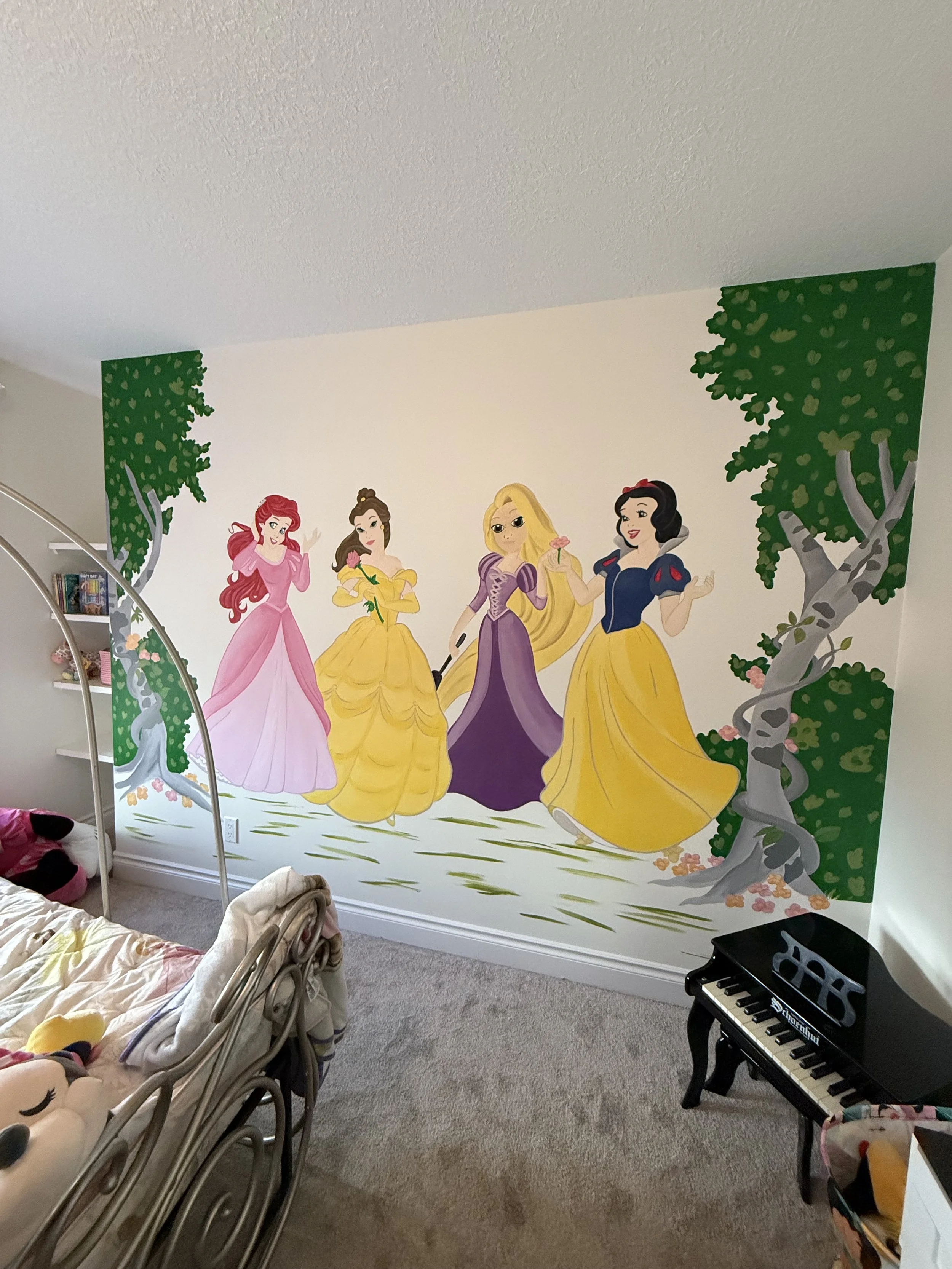Interior of a child's room with a mural of Disney princesses on the wall, including Ariel, Belle, Rapunzel, Snow White, and another princess, along with two green trees on either side of the mural. Mural by Edmonton, AB artist Carly Marie Murals