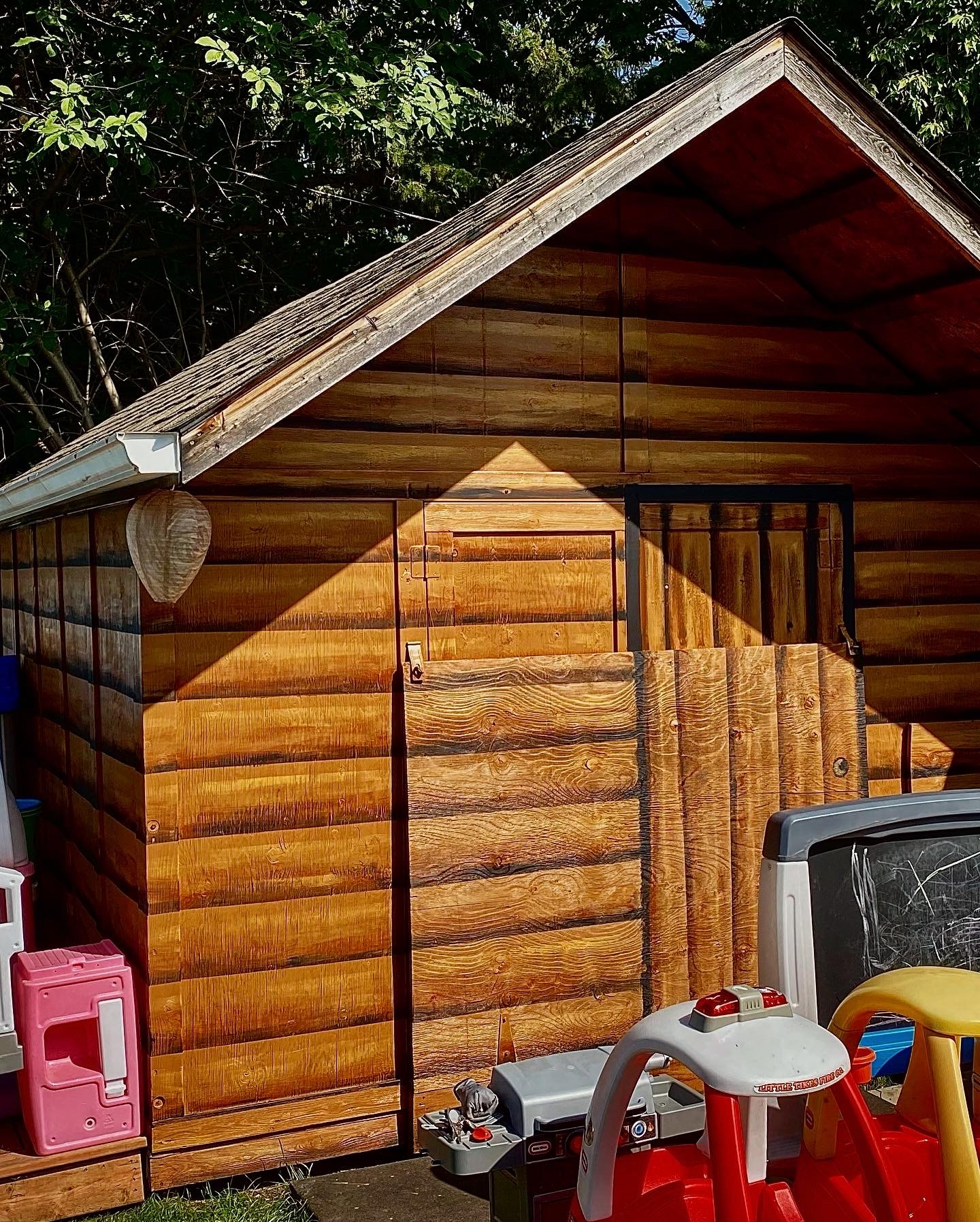 Dayhome backyard shed custom painted to look like a wood cabin illusion versus the old tired white paint. Cabin painted by Edmonton, AB artist Carly Marie Murals 