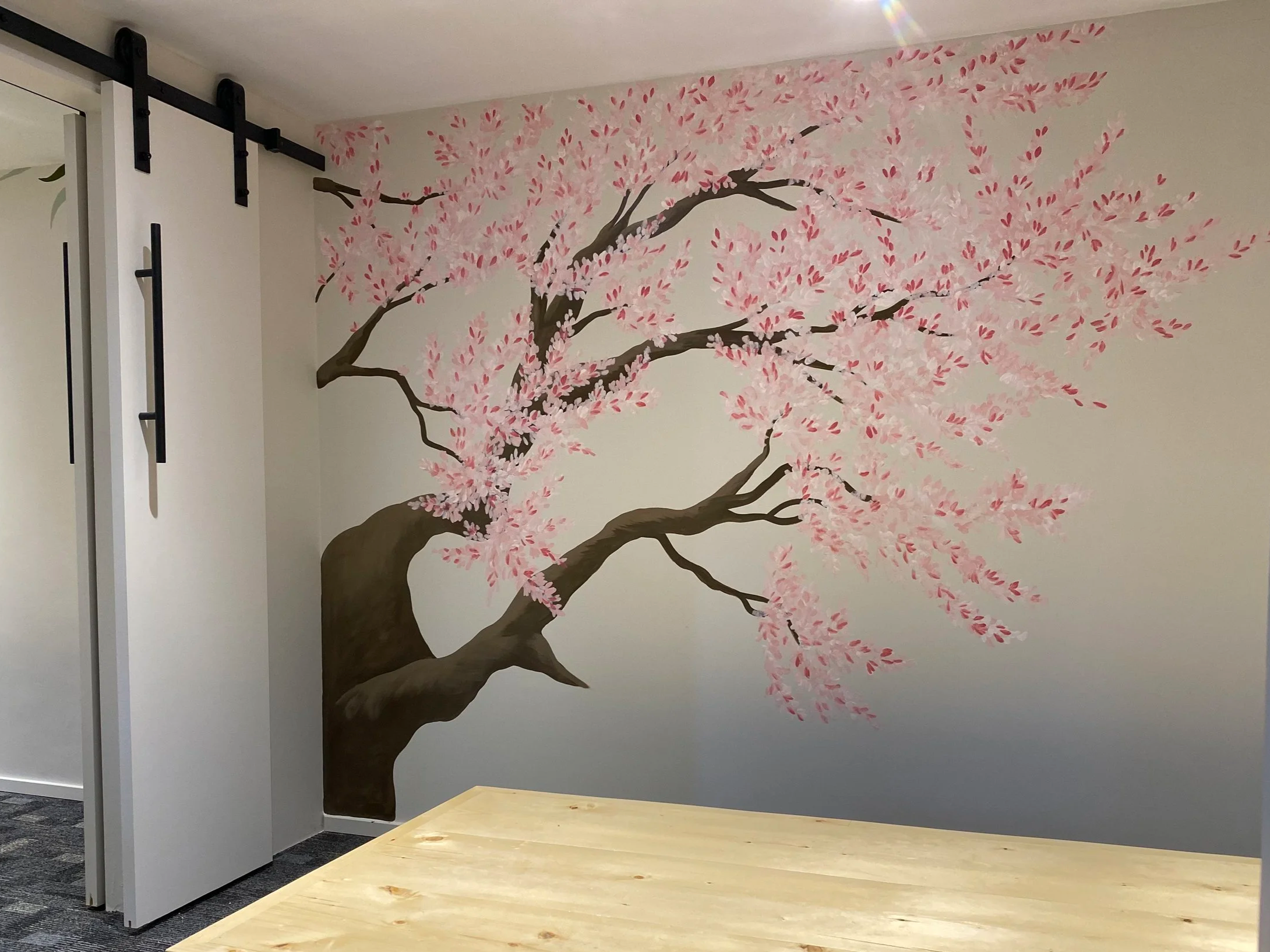A mural of a cherry blossom tree painted on a wall, with pink blossoms and dark brown branches.