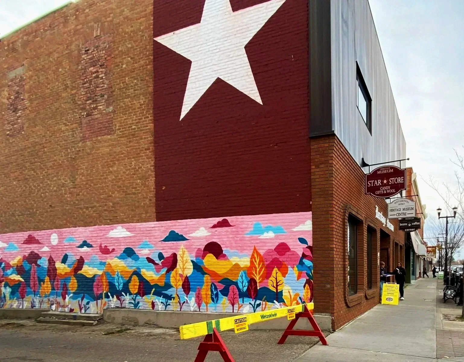 Colorful mural painted on the side of Wetaskiwin Heritage Musuem, a brick building featuring vibrant landscape with trees and clouds below by Edmonton artist Carly Marie Murals