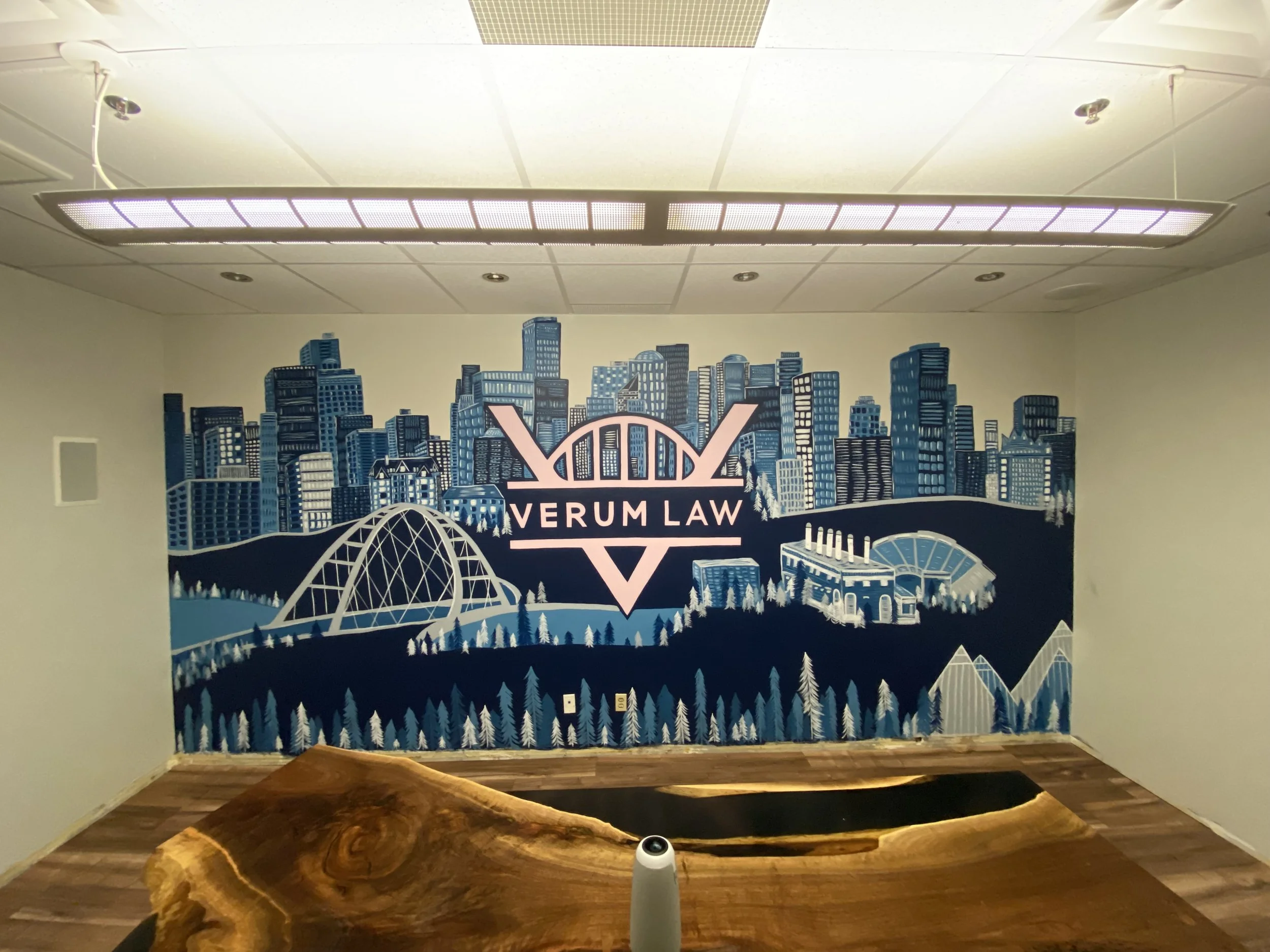 Indoor mural of a city skyline with a large arch bridge, trees, and the words "Vervum Law" in the center.